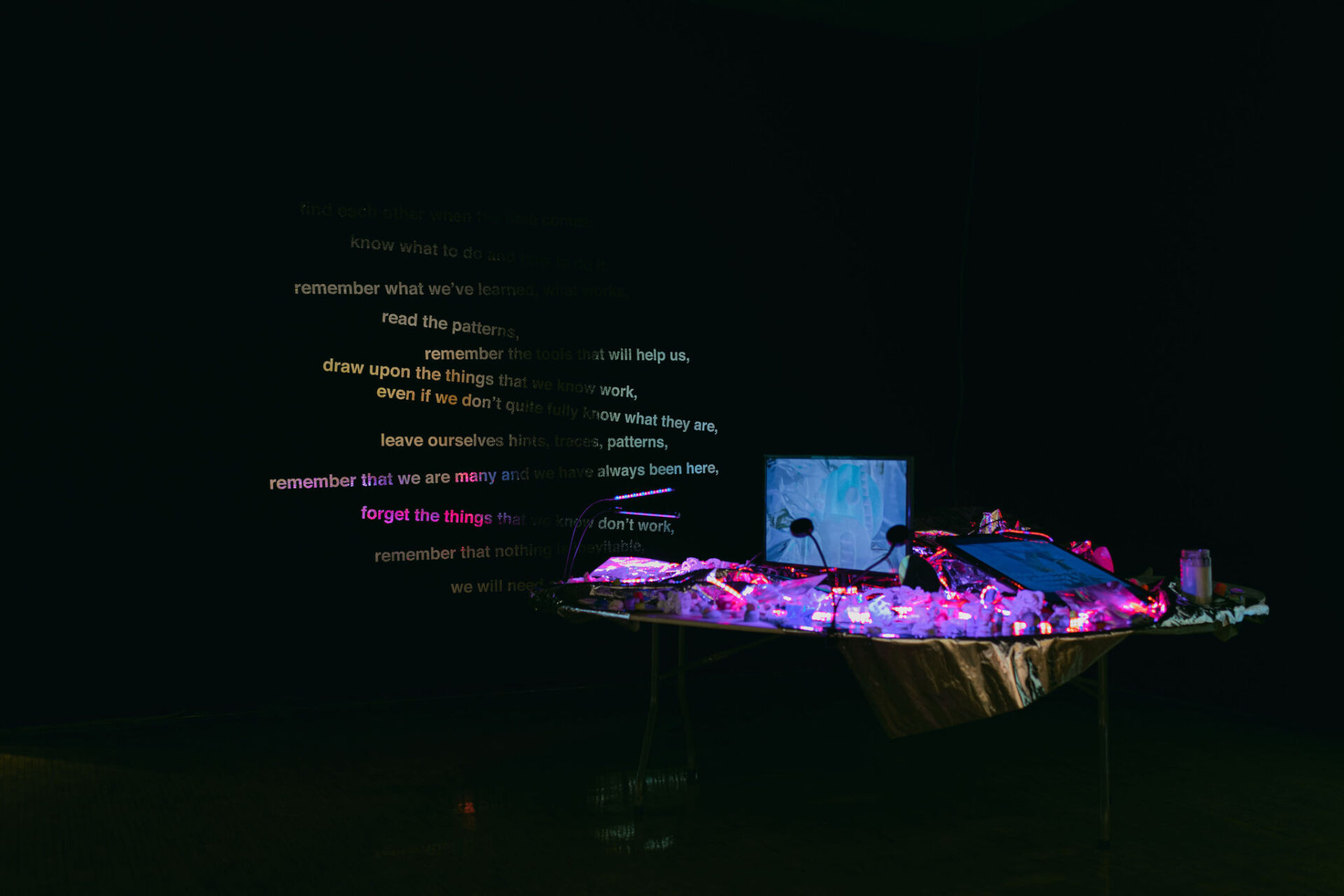 Dark room with glowing text on the wall and a neon-lit installation