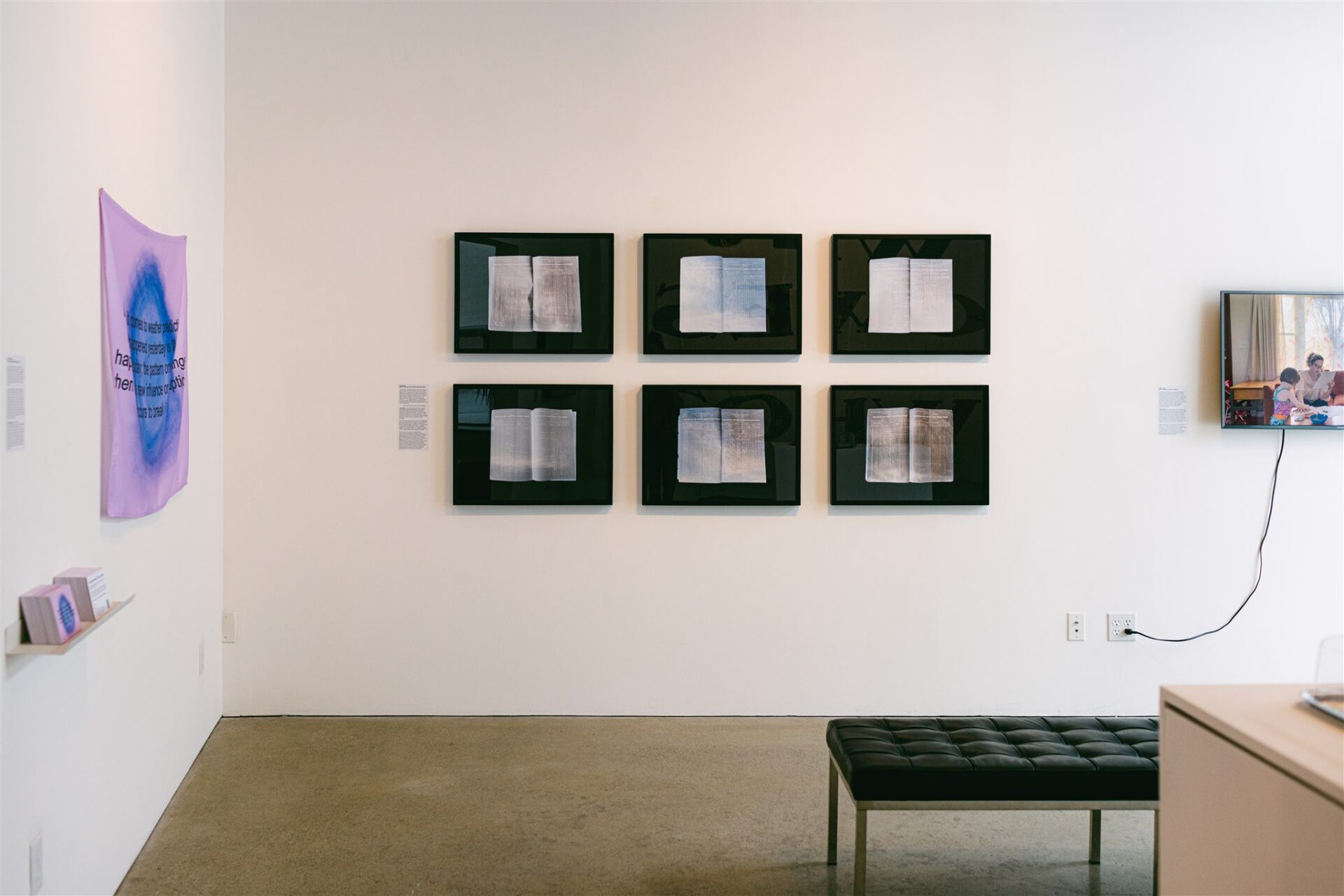 Framed book scans, purple text art, and a video screen in a gallery