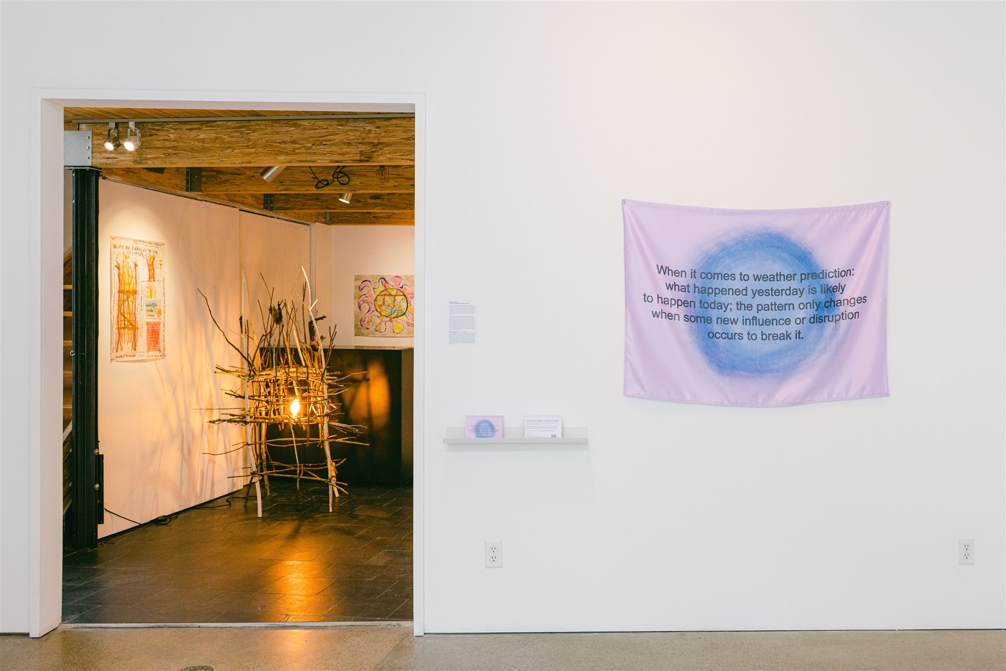 Text banner and view into a room with twig sculptures and wall art