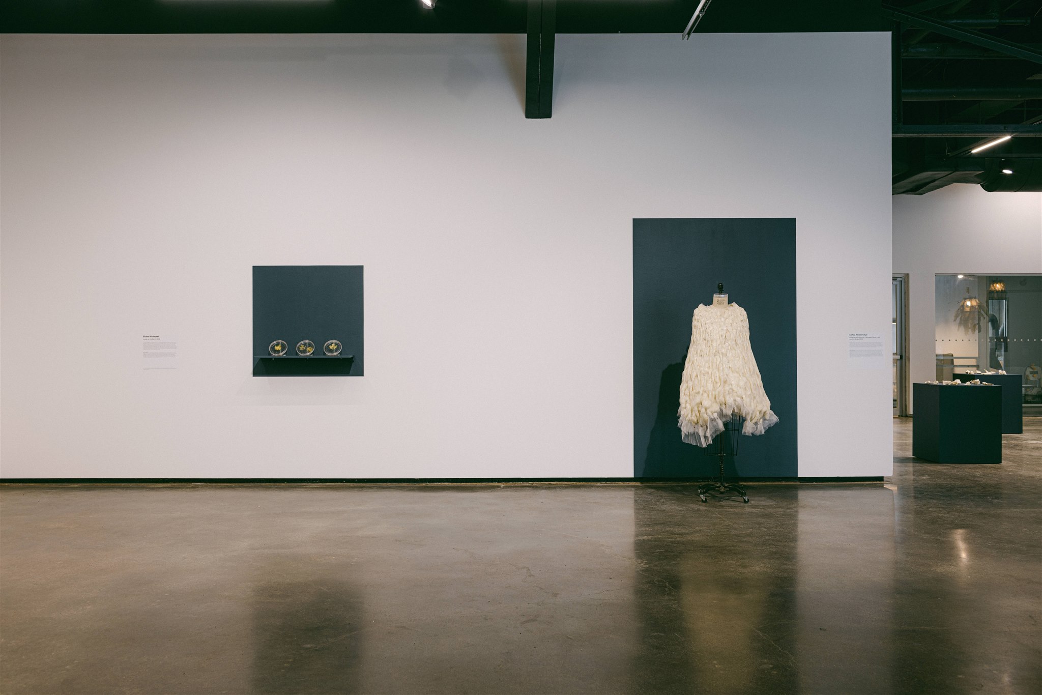 Wall display with three glass pieces and a white textured dress on a mannequin