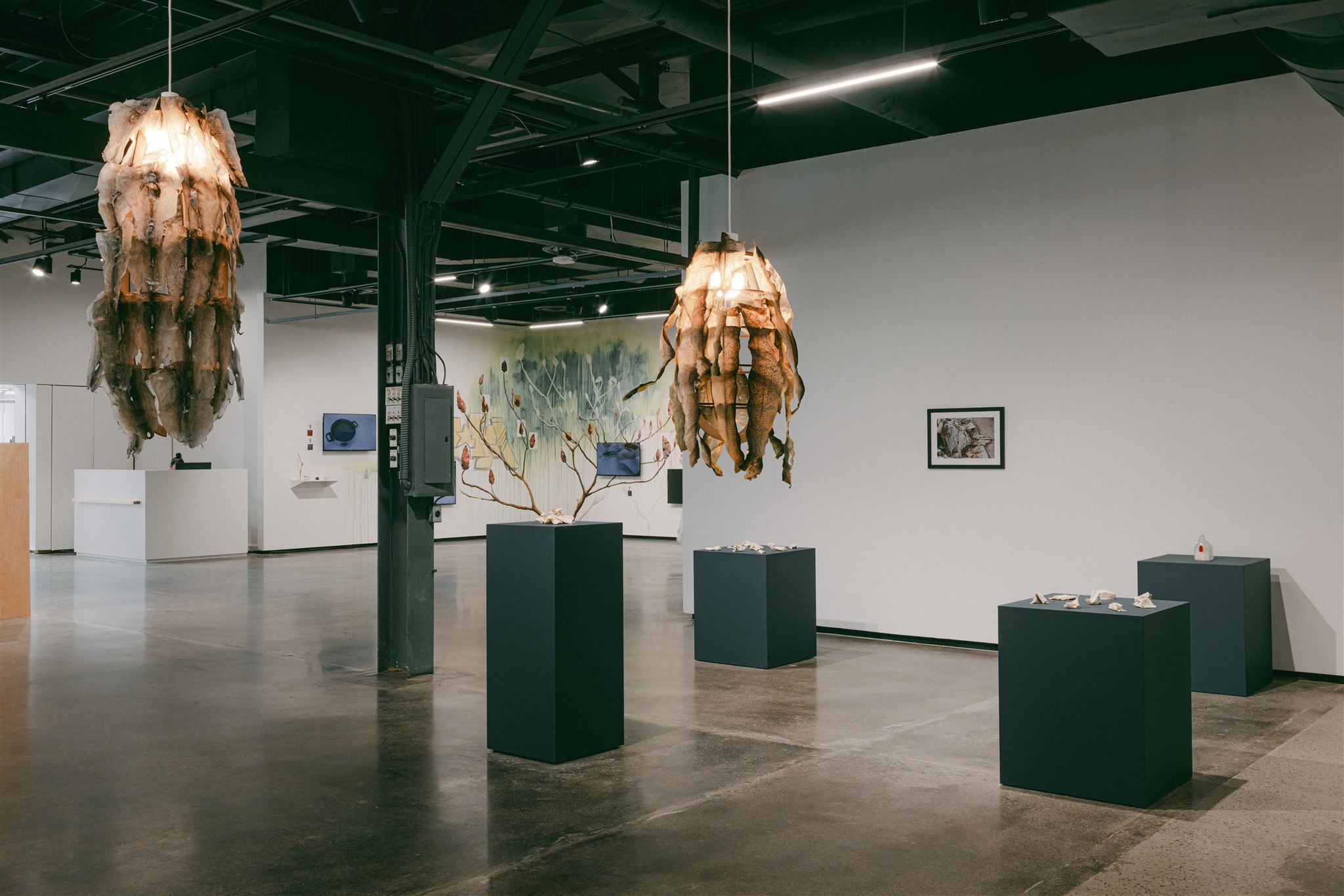 Hanging sculptures and pedestal displays in a gallery with art on the walls
