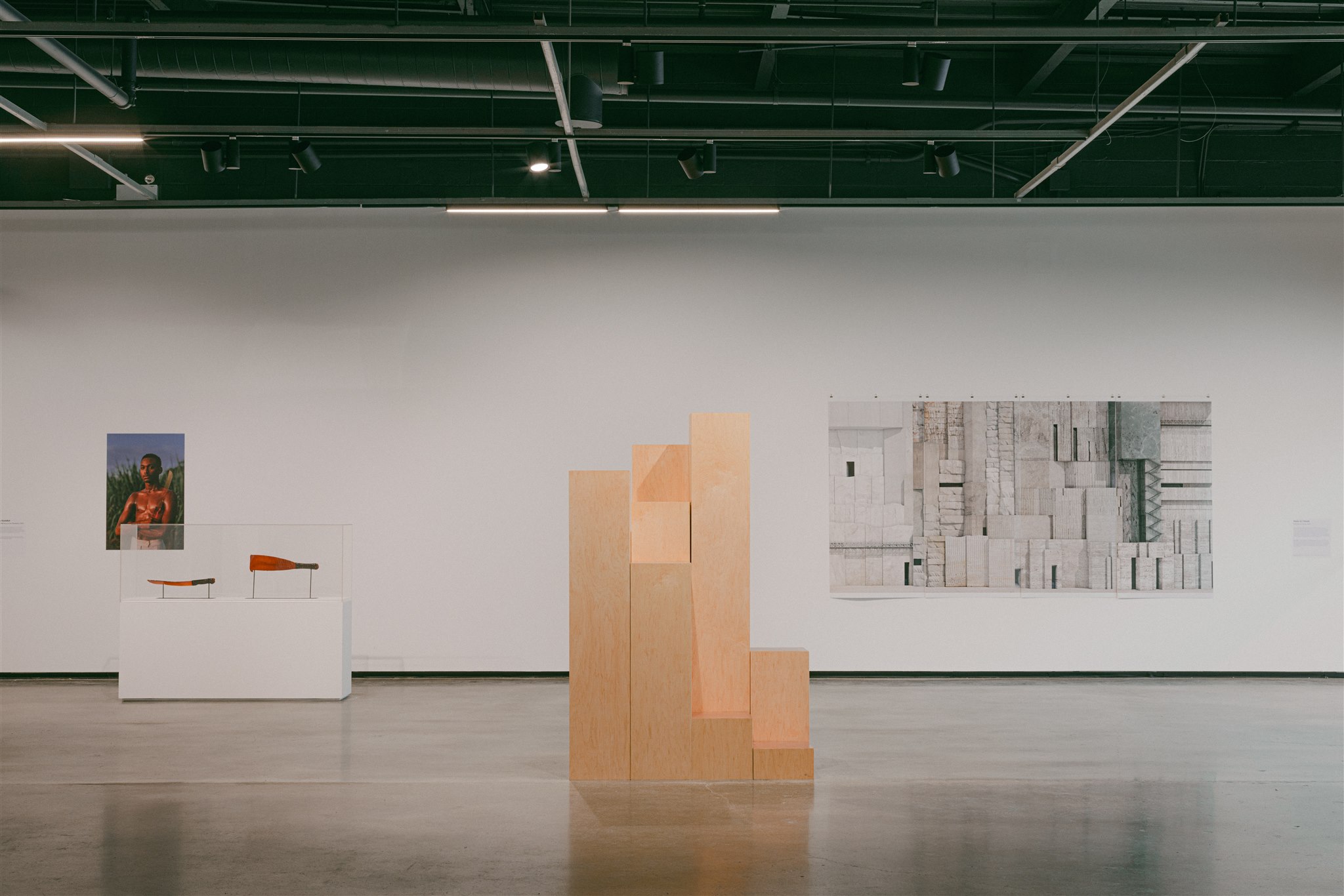 Monolithic wood sculpture in front of machetes display and a large grayscale wall piece