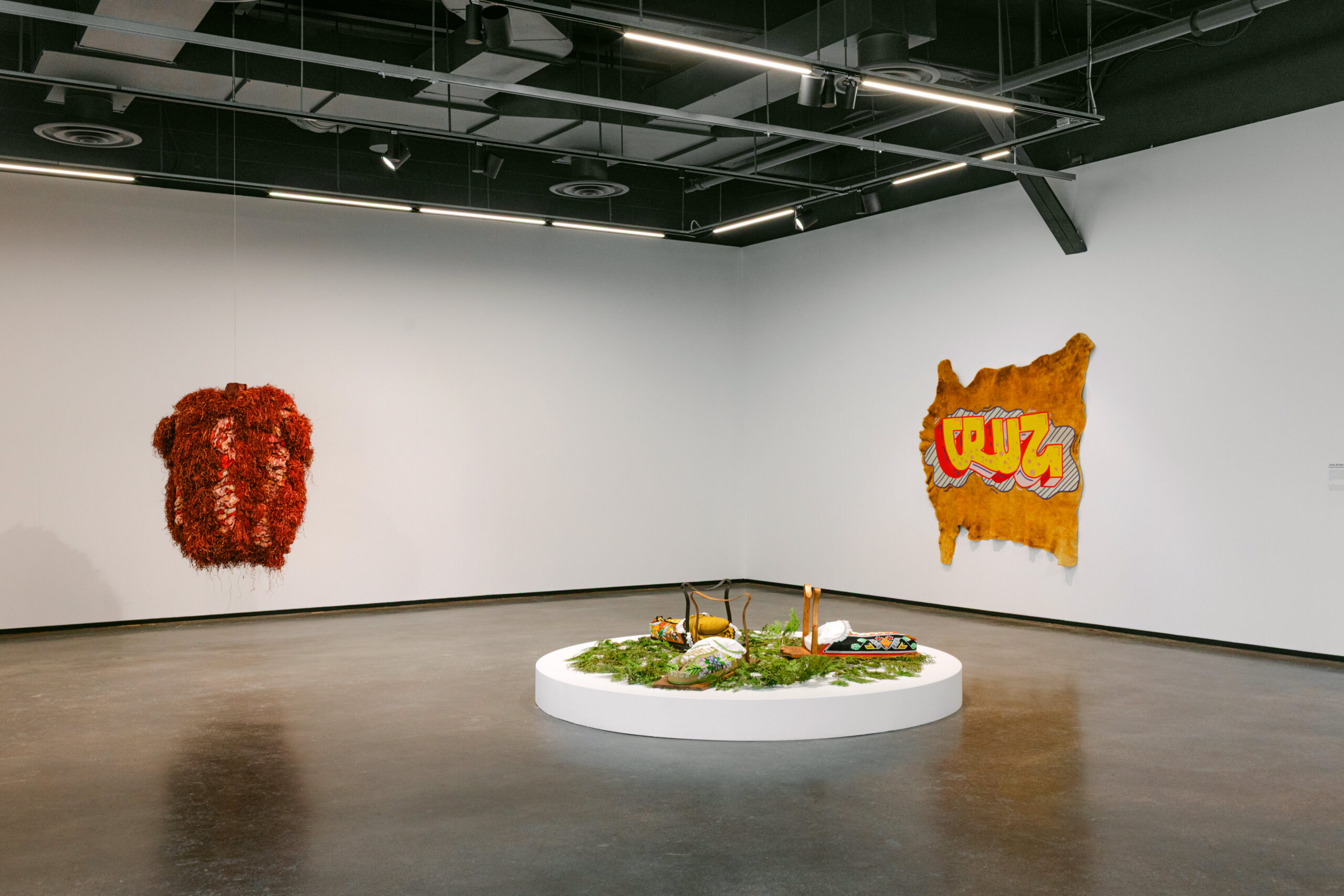 Gallery with a round nature display, red hanging sculpture, and hide with graffiti text 'CRUZ