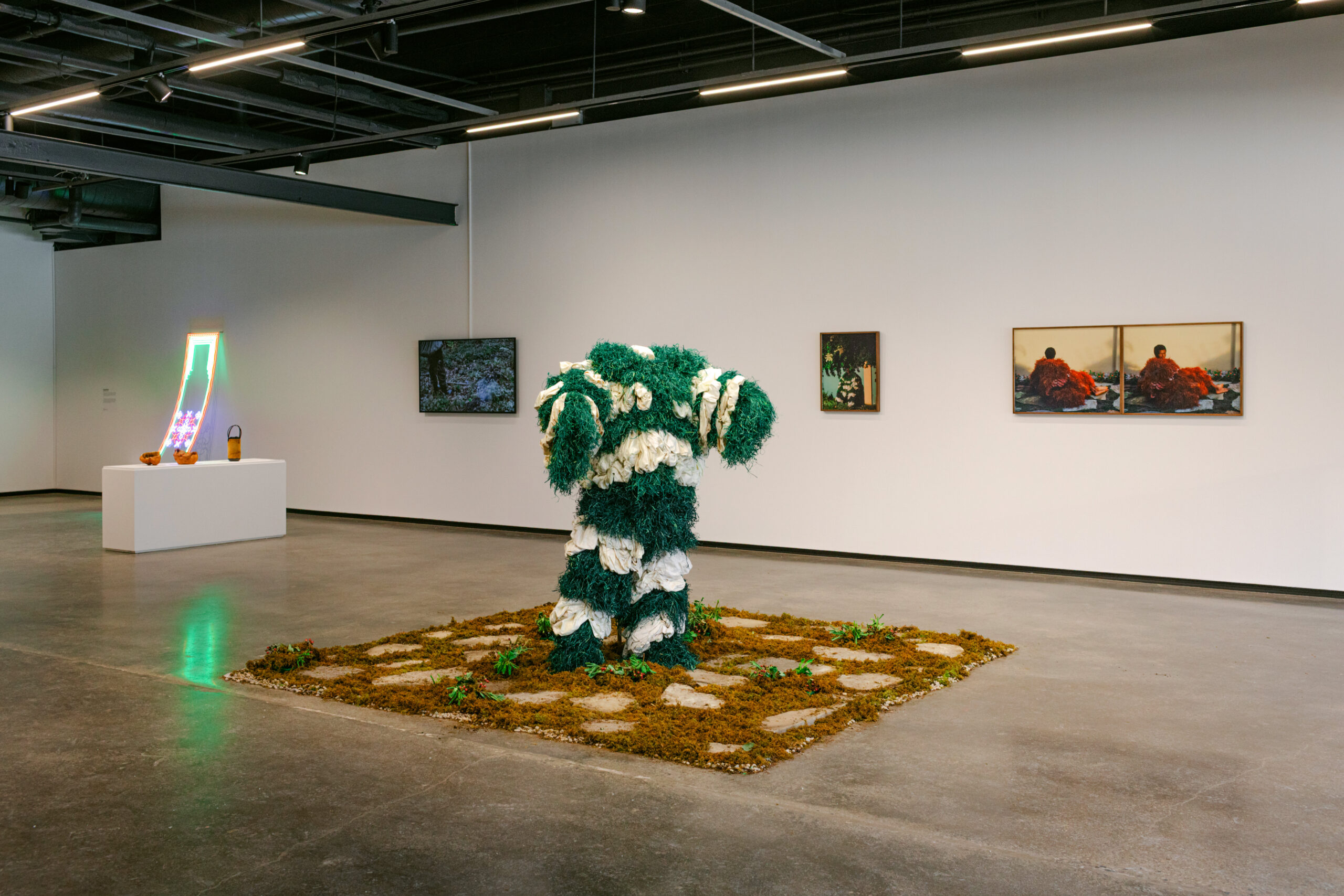 Green and white fiber sculpture with surrounding photos and neon artwork in a gallery