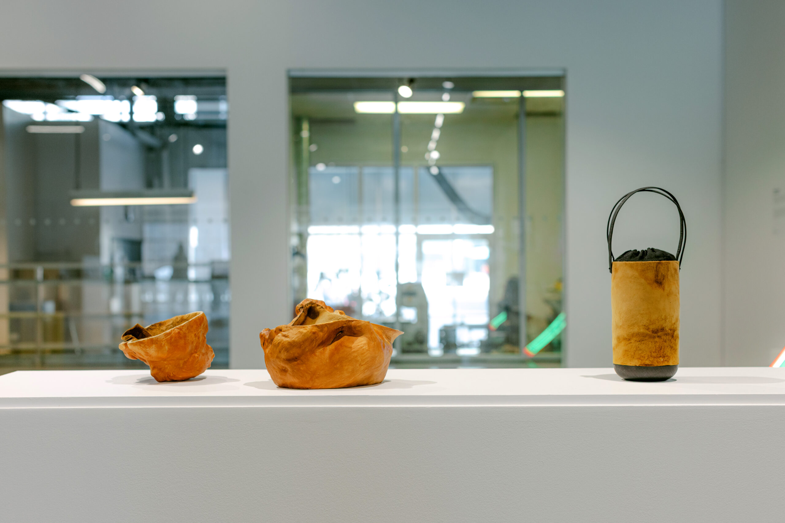 Three vessels on a white pedestal in a gallery setting