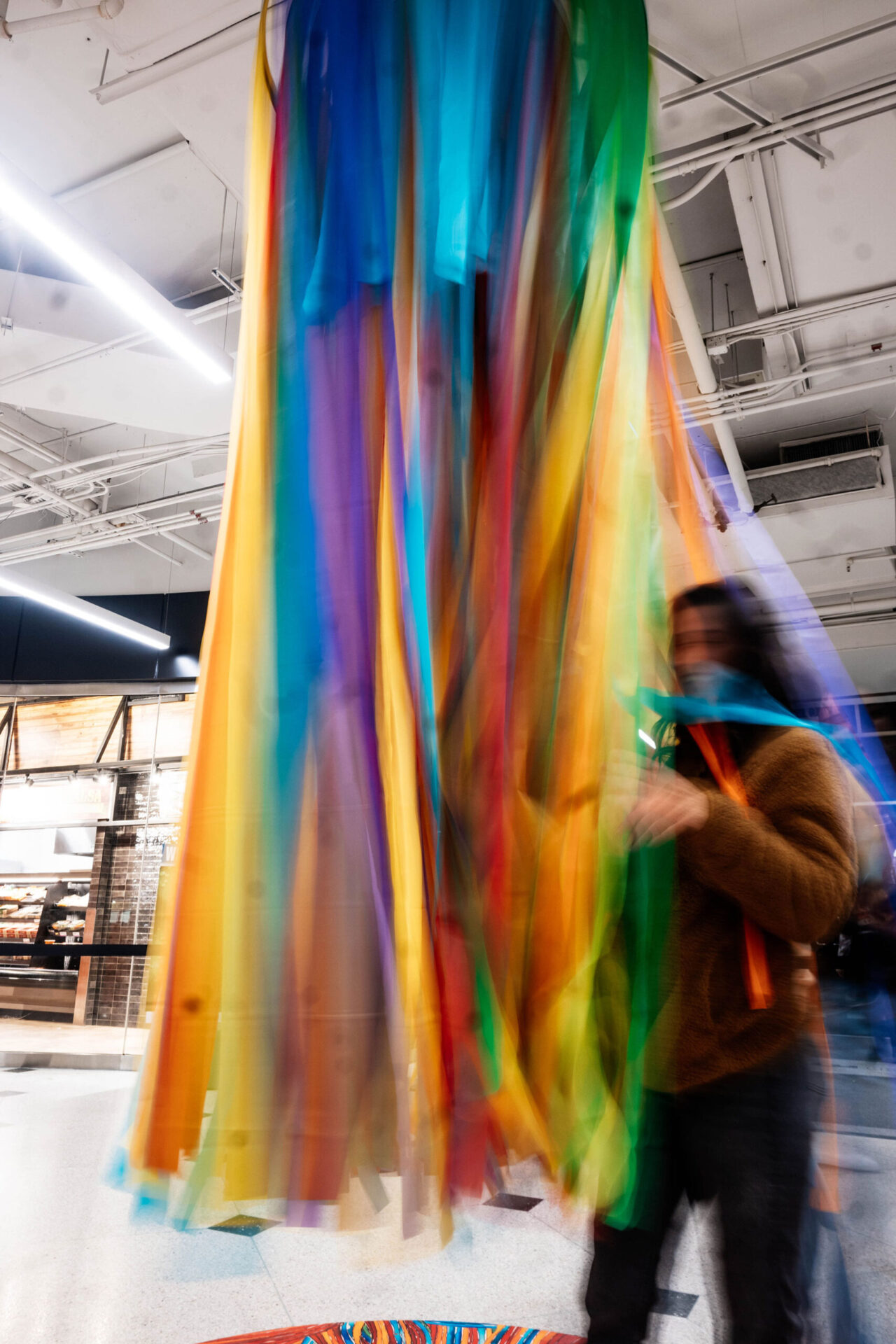 a woman is smiling about to enter the cluster of multicoloured ribbons coming from ceiling. The image is blurry as if in flow