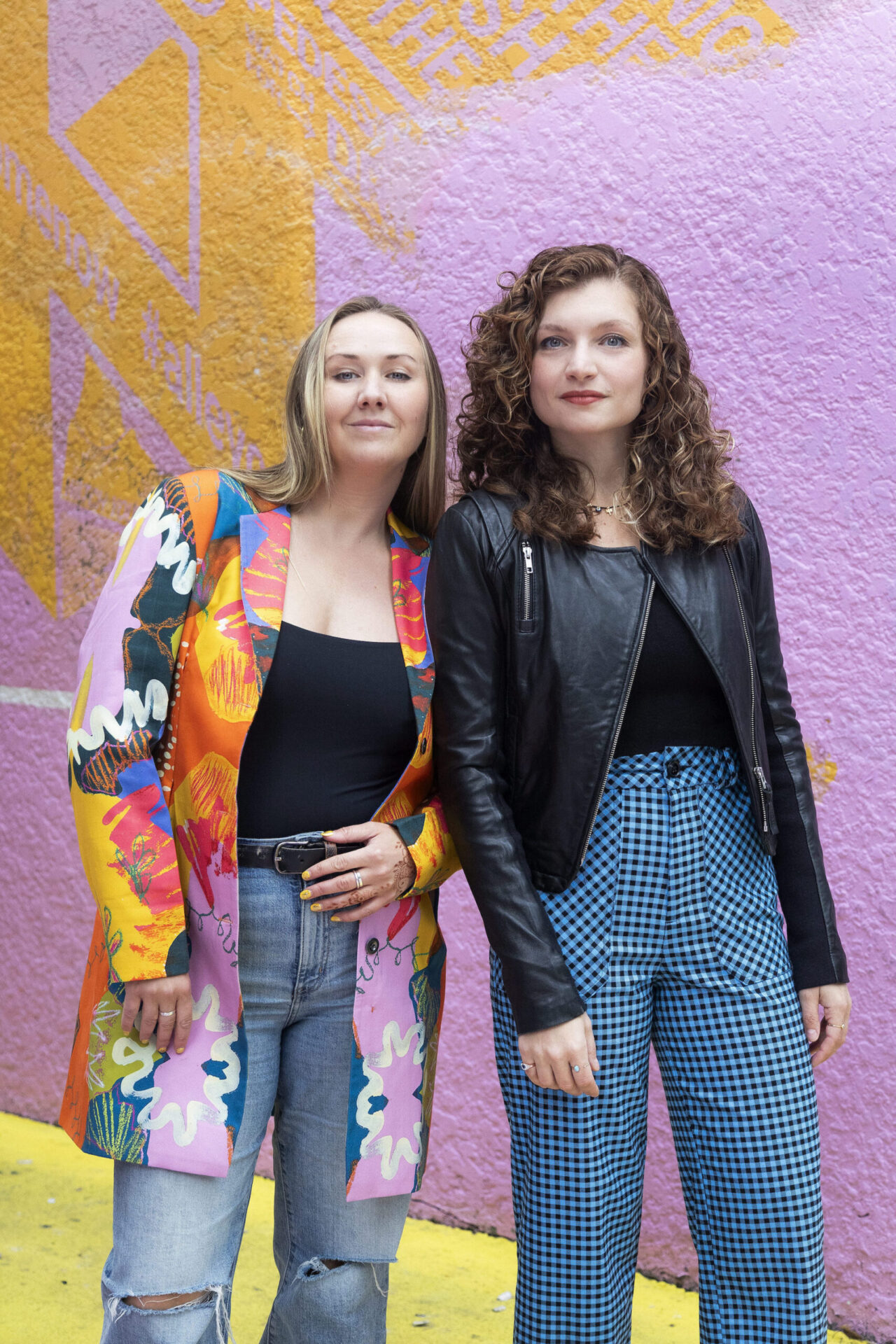 photo of two women standing in a bright yellow and purple setting