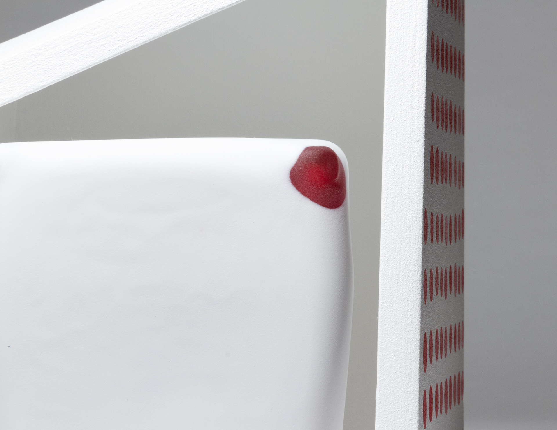 A detail of a white and red glass cube inside a white wood artwork with painted red dots on the right side.