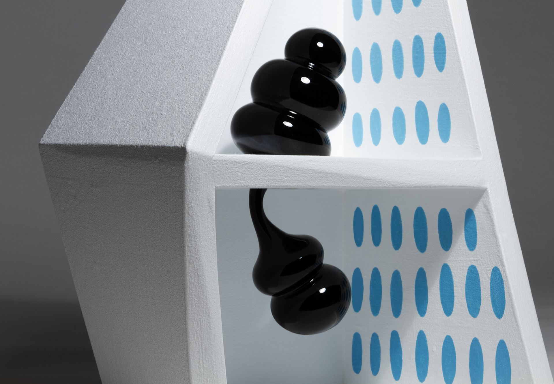A detail of a black glass form inside a white wood artwork with blue ovals inside the right wall.