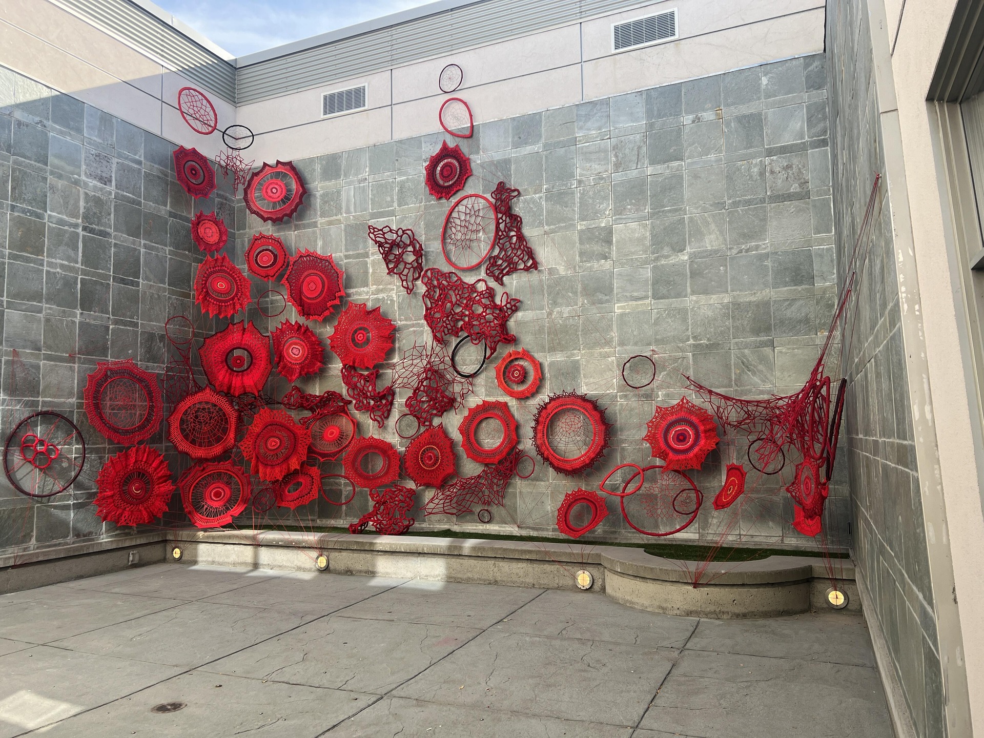Red art installation created with round weavings with crochet around the edges on the courtyard wall which is roughly two stories high.   Kelowna Art Gallery.