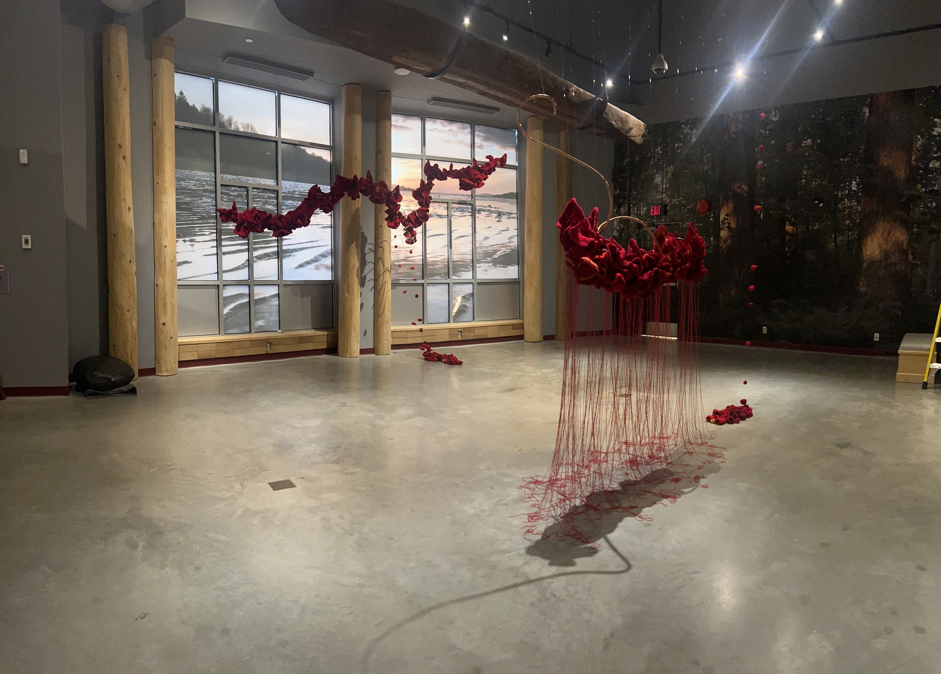 Red art installation at the Museum of Surrey.  Suspended large crochet piece which mirrors the large canoe which is also suspended from the ceiling.  Large crochet pieces are also suspended in front the large windows.  the crochet pieces mirror the large photo of waves that has been used to cover the windows.