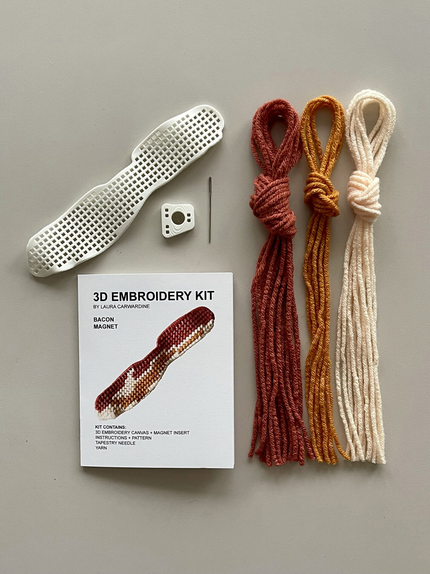 Embroidery Kit Contents on a tabletop showing a booklet, canvas, needle, and yarn