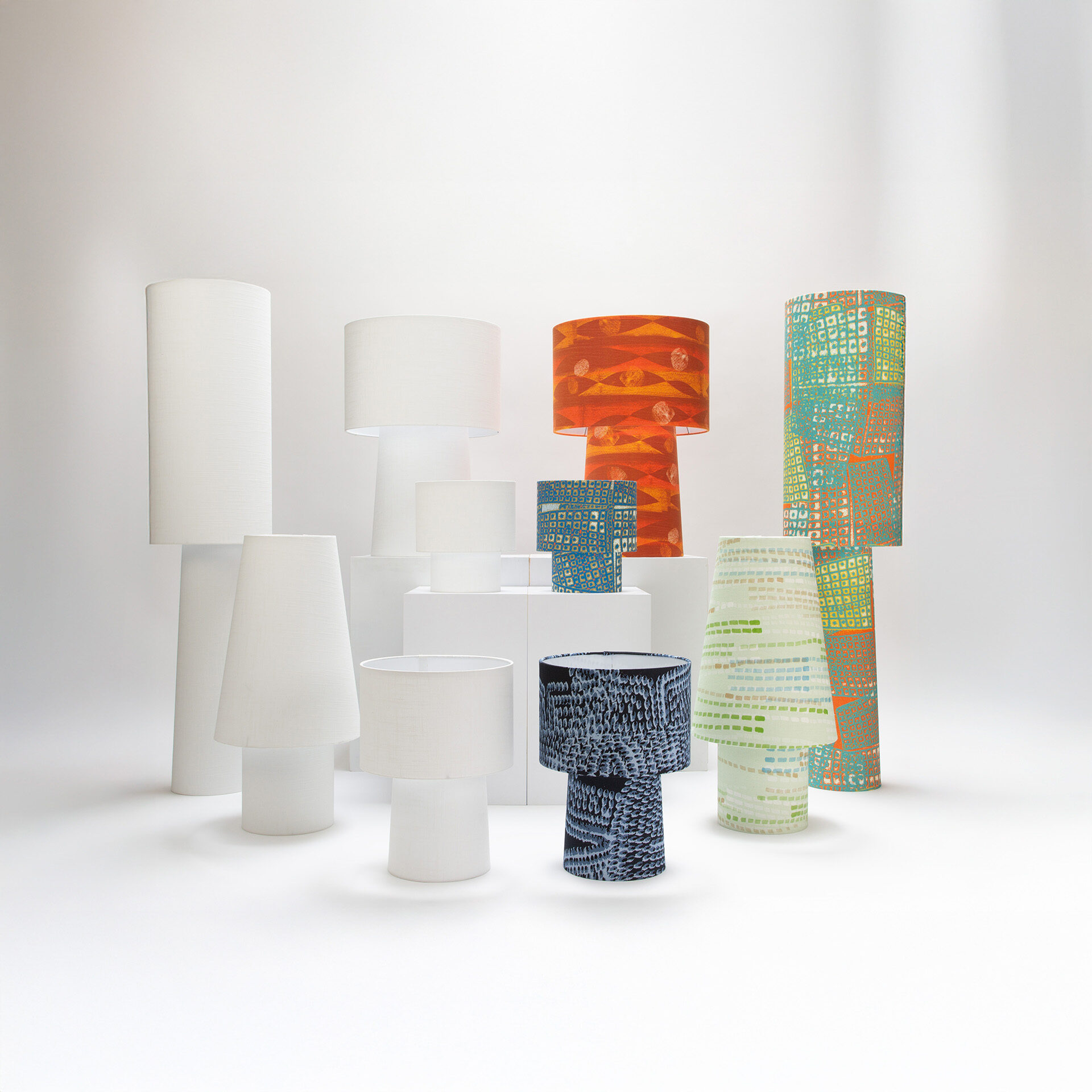 min/max lamp collection by Jenny San Martin showing five lamp styles in both white linen and colorful patterned versions including orange, turquoise, blue, and green designs from the Ampli collection