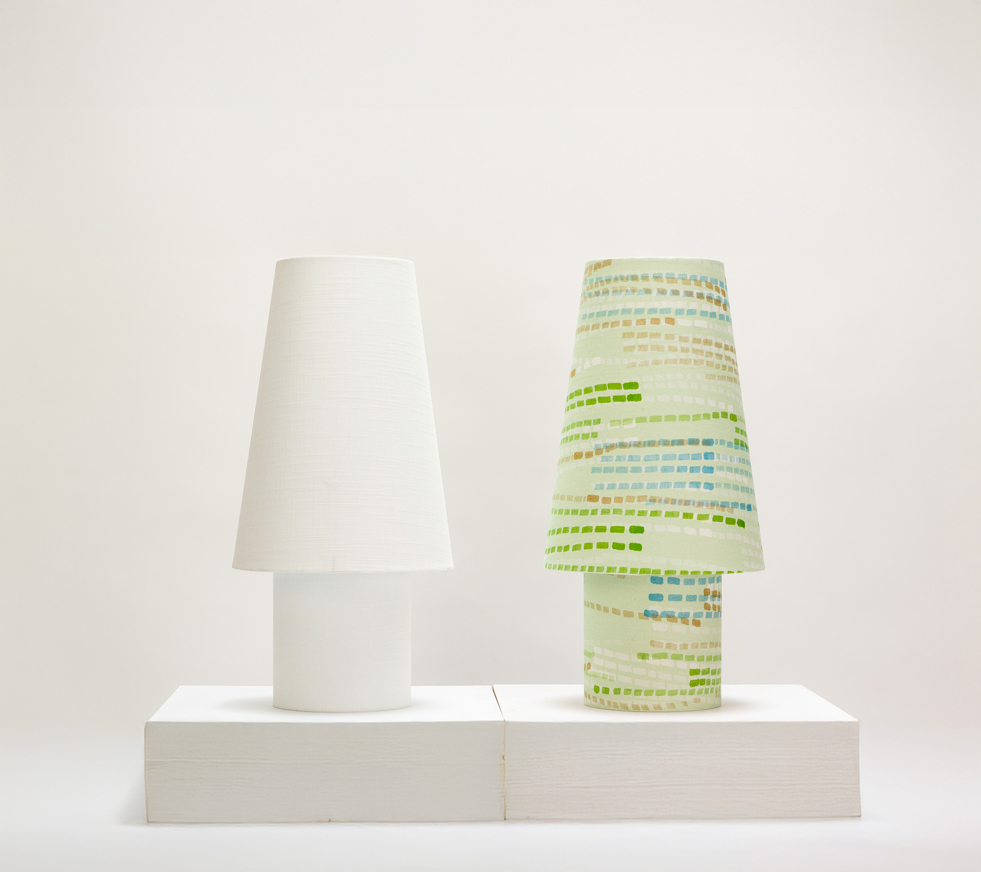 Side-by-side comparison of min/max table lamps: white textured linen version next to patterned version with green and blue geometric pattern from the Ampli collection