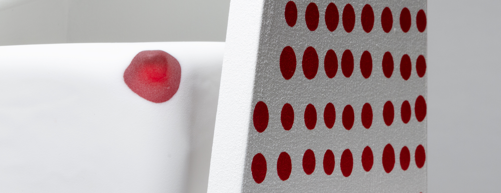 A detail of a white and red glass cube inside a white wood artwork with painted red dots on the right side.