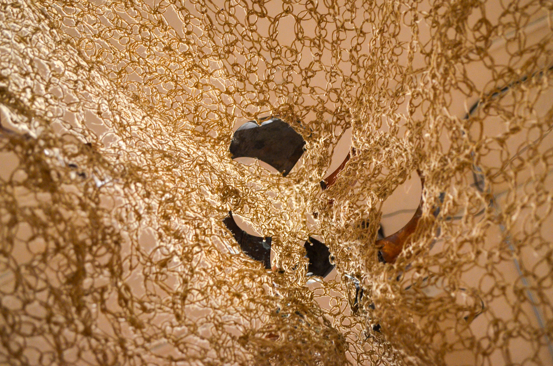 The image depicts a handwoven textile mesh made from hemp that contains fragments of organically shaped copper.
