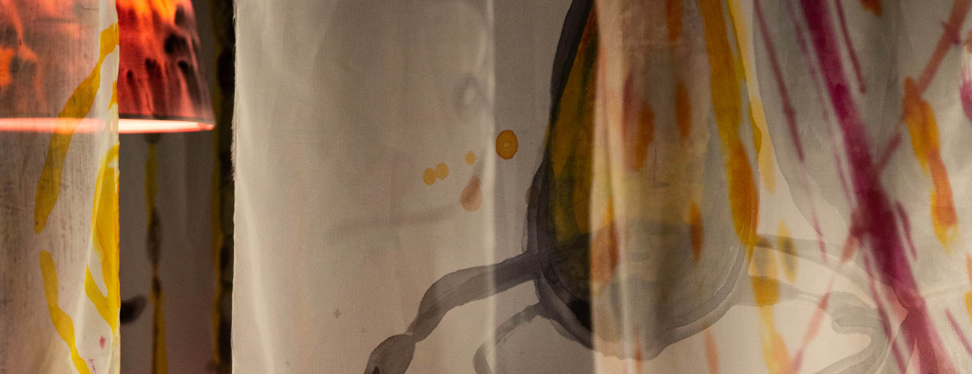 A black, yellow, and pink lamp shines behind a sheer curtain with a chalice painted onto it