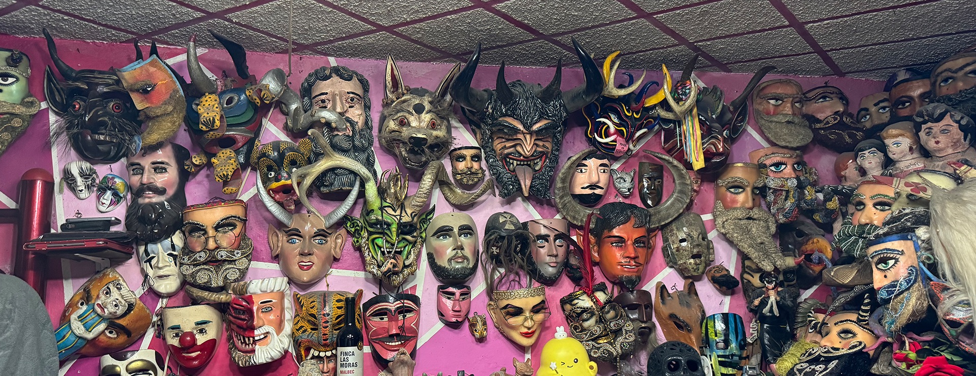 Image of a purple wall filled with handmade masks painted in a variety of colours. 