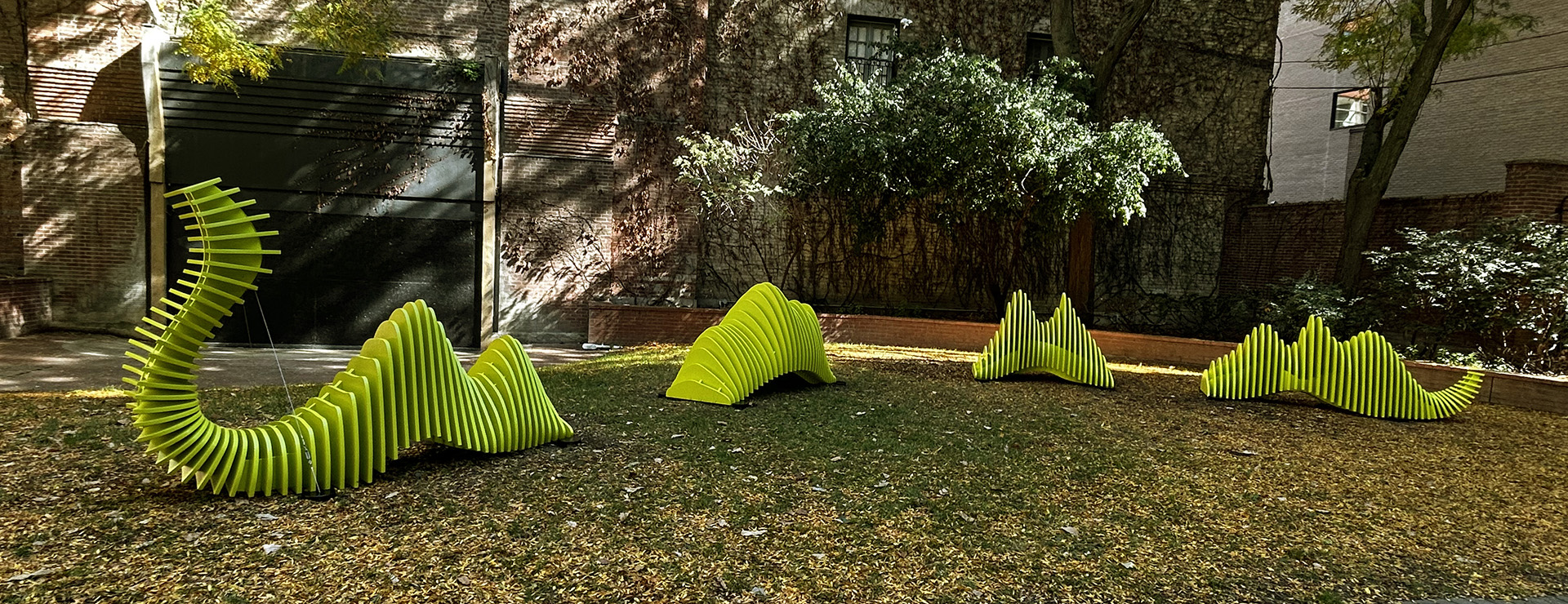 A serpent-like sculpture coming in and out of a grassy park. The serpent is lime green and has ridges resembling audio waves.