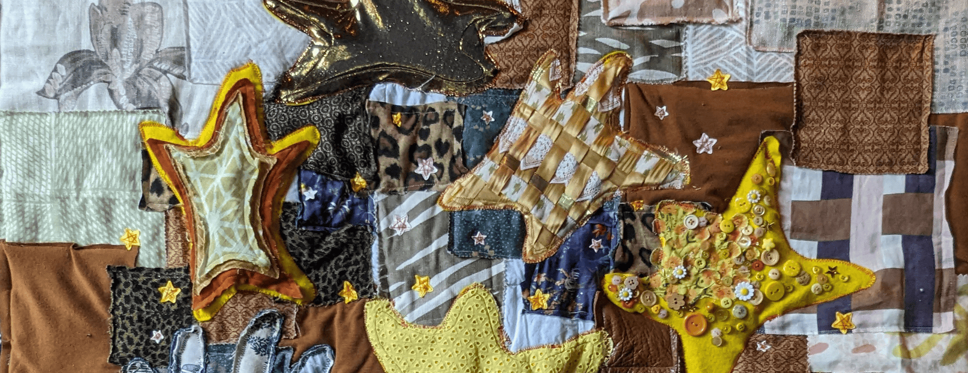 Five yellow, orange, and gold stars sewn on top of a patchwork background