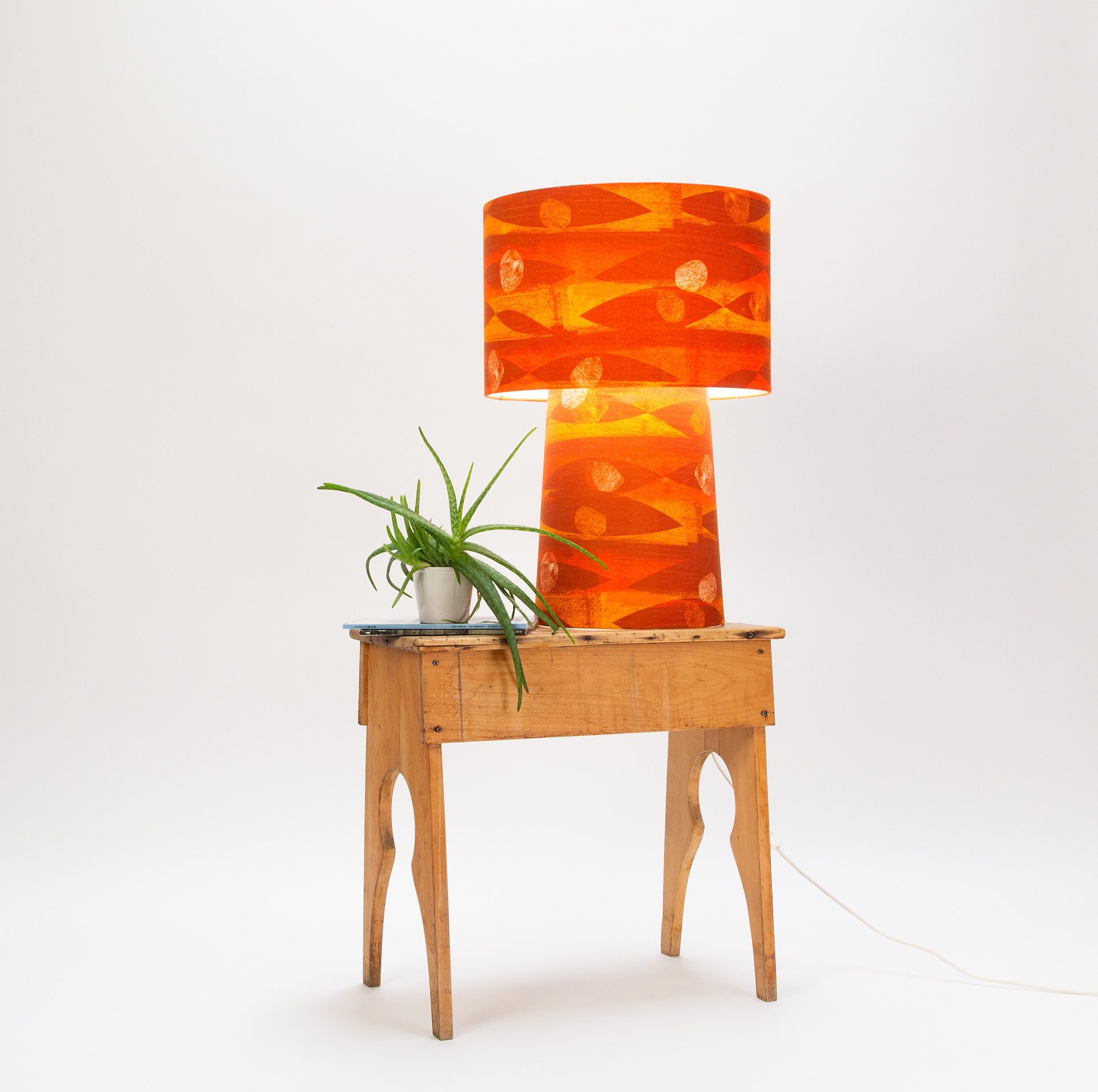 Illuminated orange and yellow patterned table lamp from the min/max collection with Flame pattern, displayed on vintage wooden table with air plant