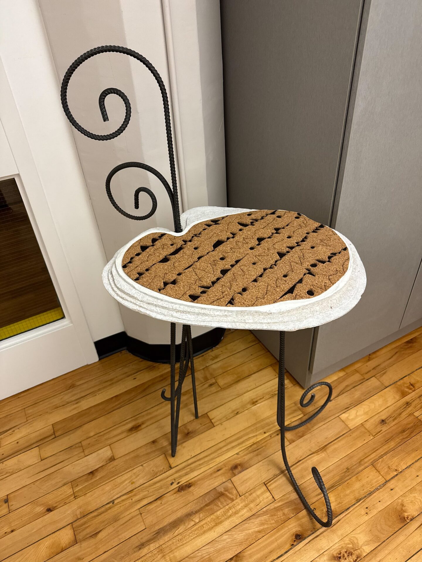 Image of a side table with bent metal coming up above to create hooks. There is a cork surface with a pattern on it. 