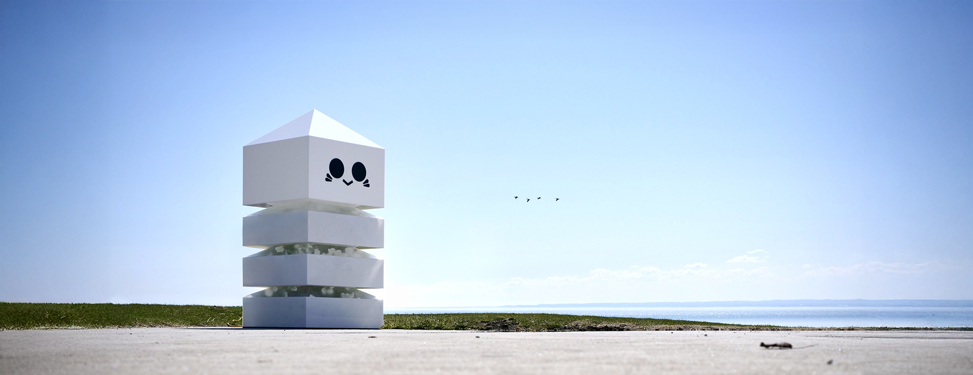 A 3 tiered installation with a calm face stands in front of a lake with a clear blue sky. 