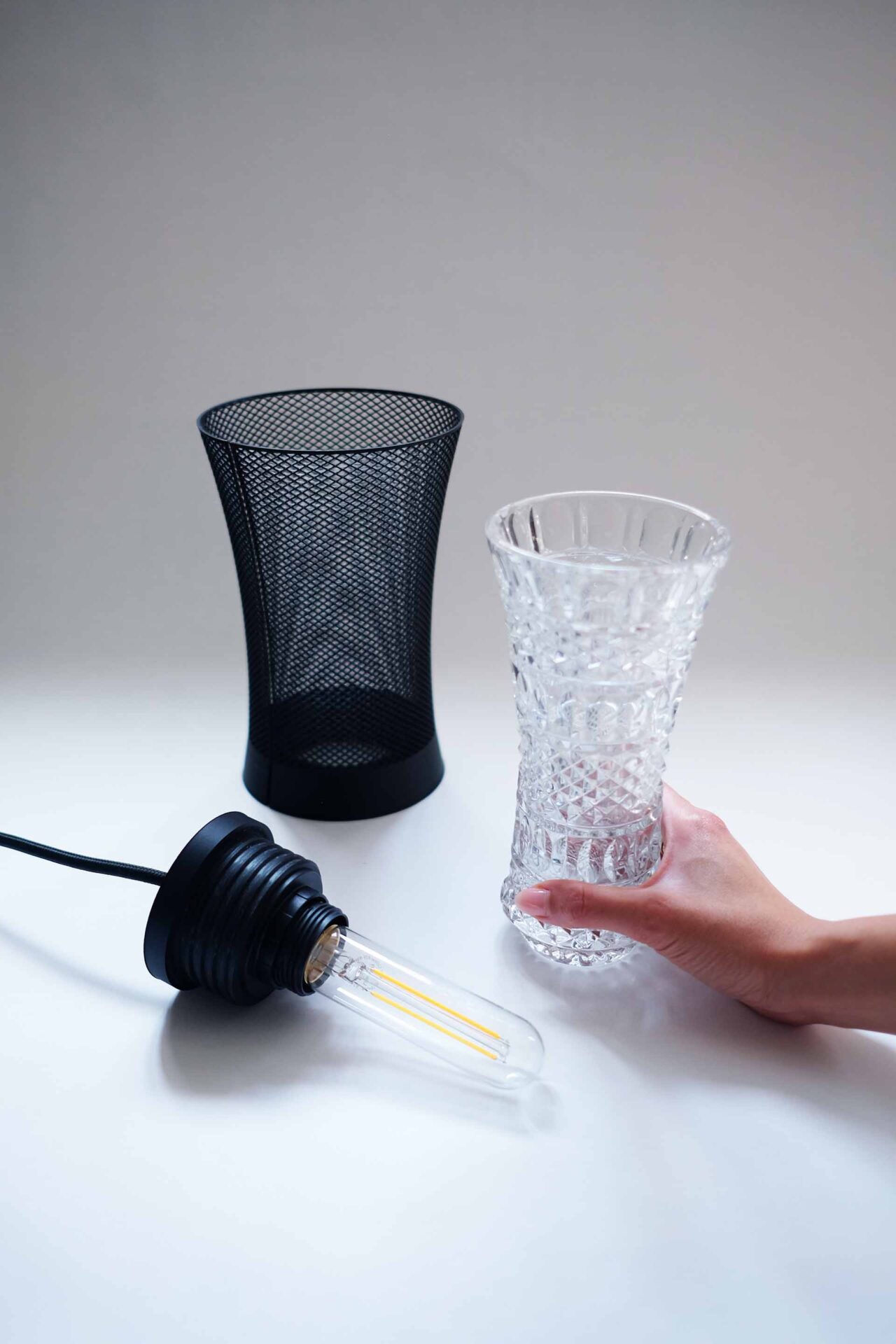 A lamp disassembled, with a hand holding the vase and the 3D print mesh beside.