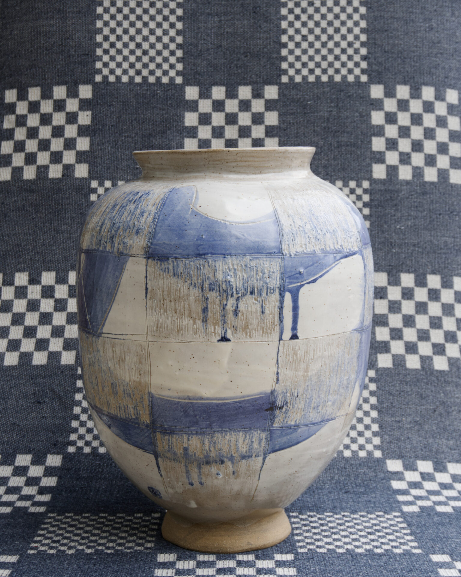 A blue and white ceramic vase on a checked blue and white textile background, viewed from face-on.