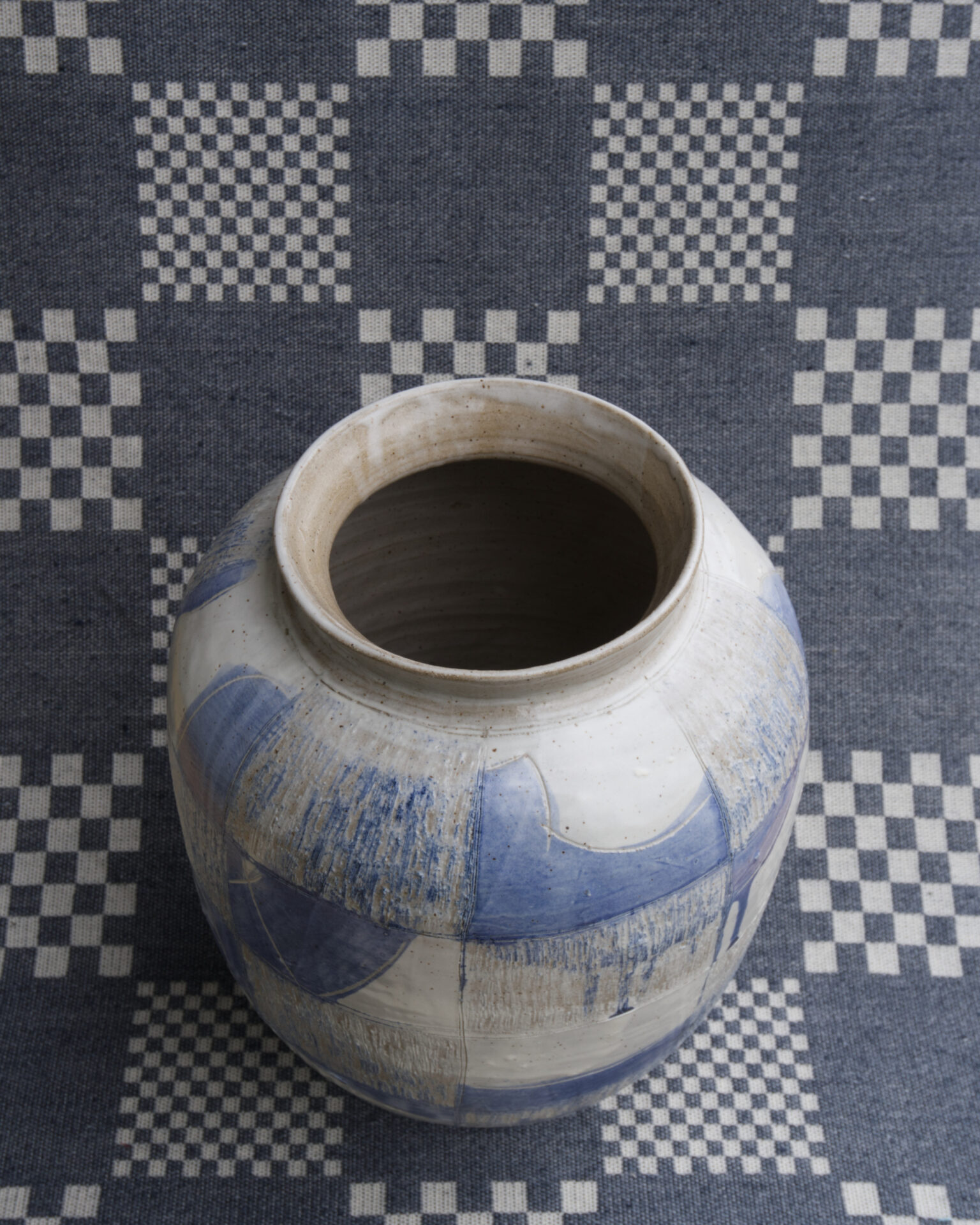 A blue and white ceramic vase on a checked blue and white textile background, viewed from above. 