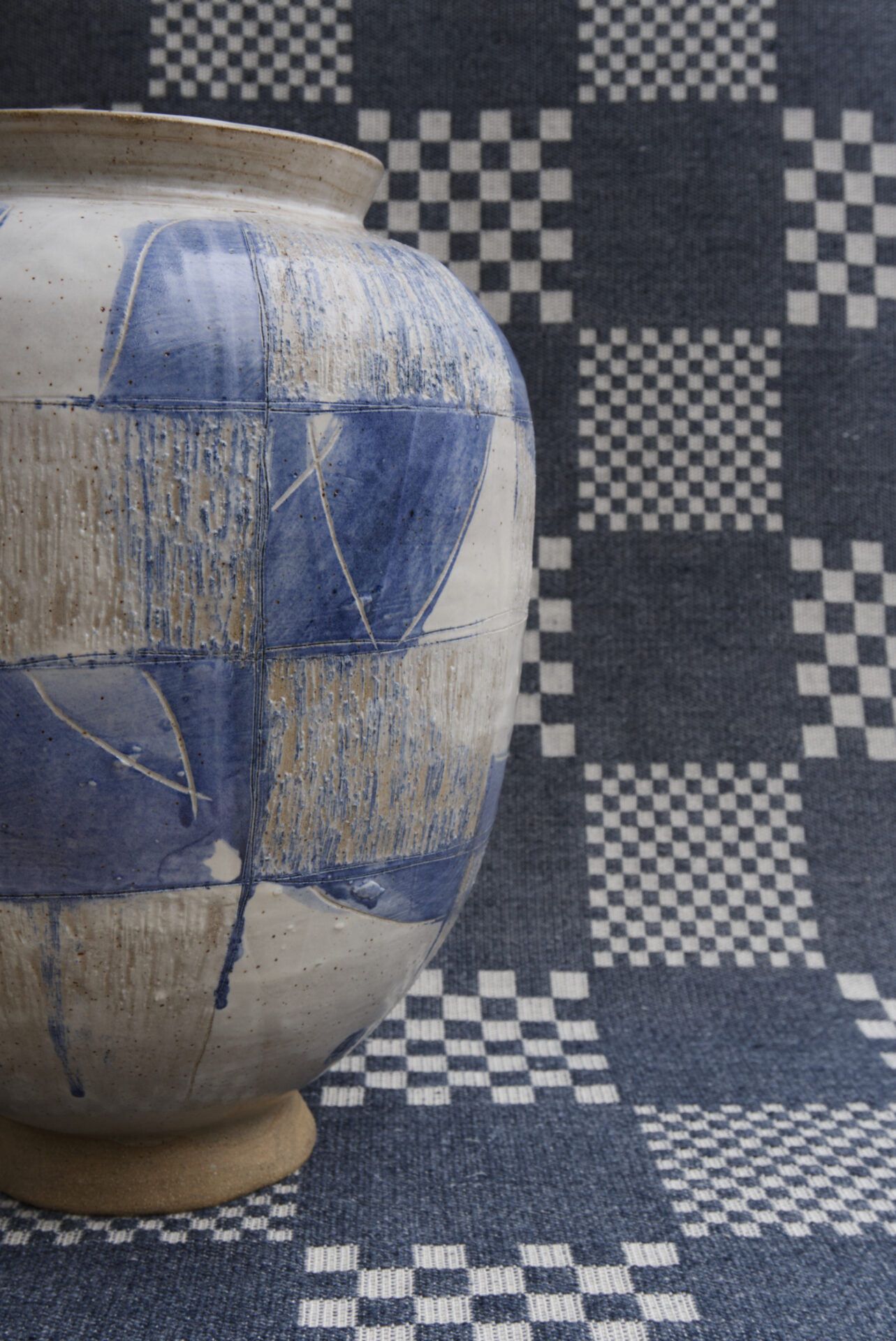 A blue and white ceramic vase on a checked blue and white textile background, viewed from the side.