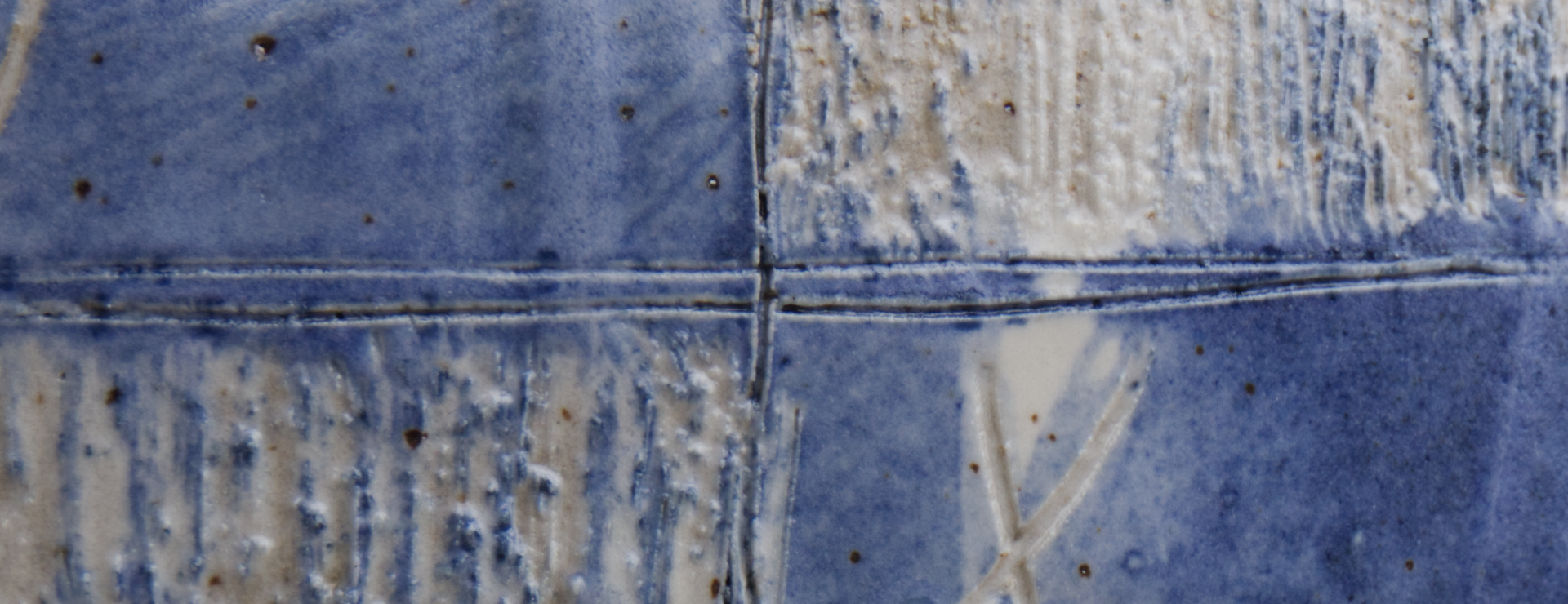 A close up of the scratched surface of a blue and white ceramic pot. 