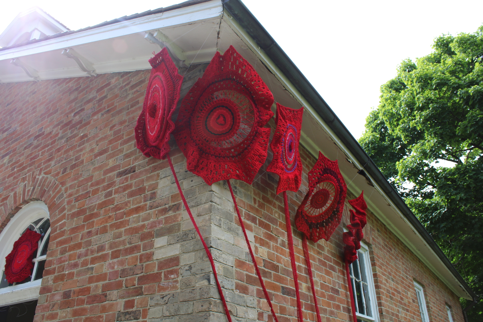 Large flowers created from crochet have been suspended on the outside of the school house at The Village at Black Creek in Toronto.  This school house is a replicant of the design by Egerton Ryerson for residential schools in Canada. 