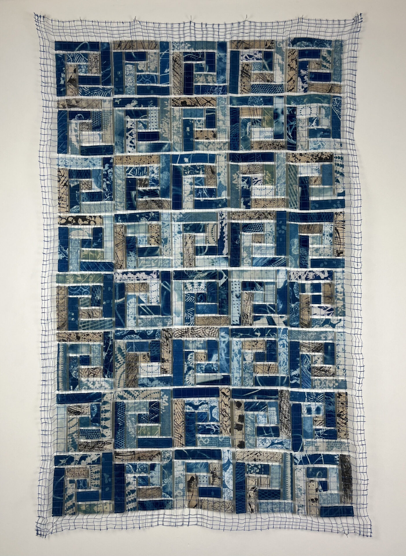 "Labyrinth", rectangular fragments of used coffee filters, patterned with cyanotype, ink and tea and sewn into a geometric pattern on an open thread grid forming a quilt-like panel.