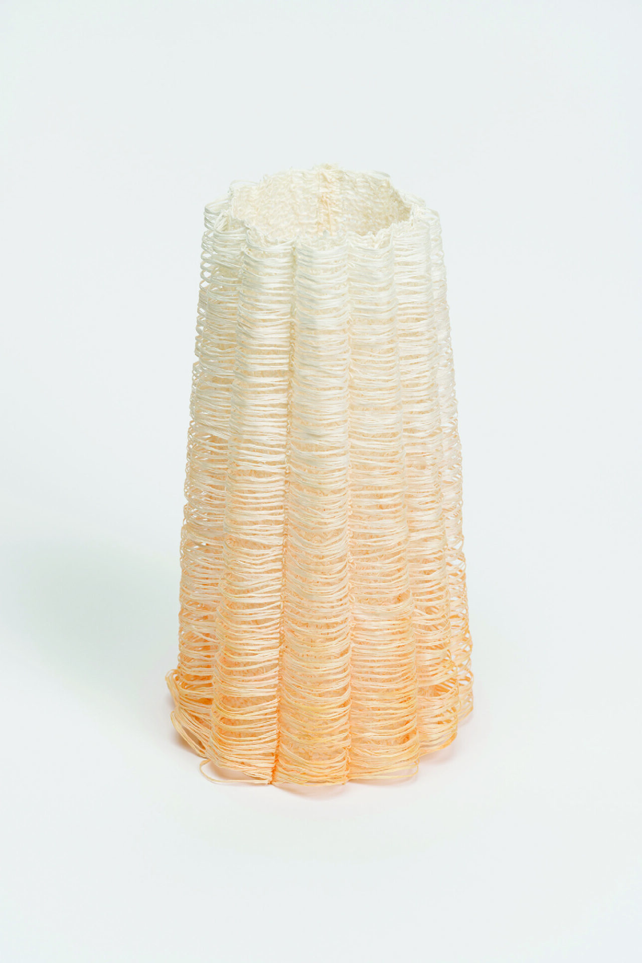 Pleated cylindrical form made of stacked translucent loops, cream-to-apricot gradient, on white.