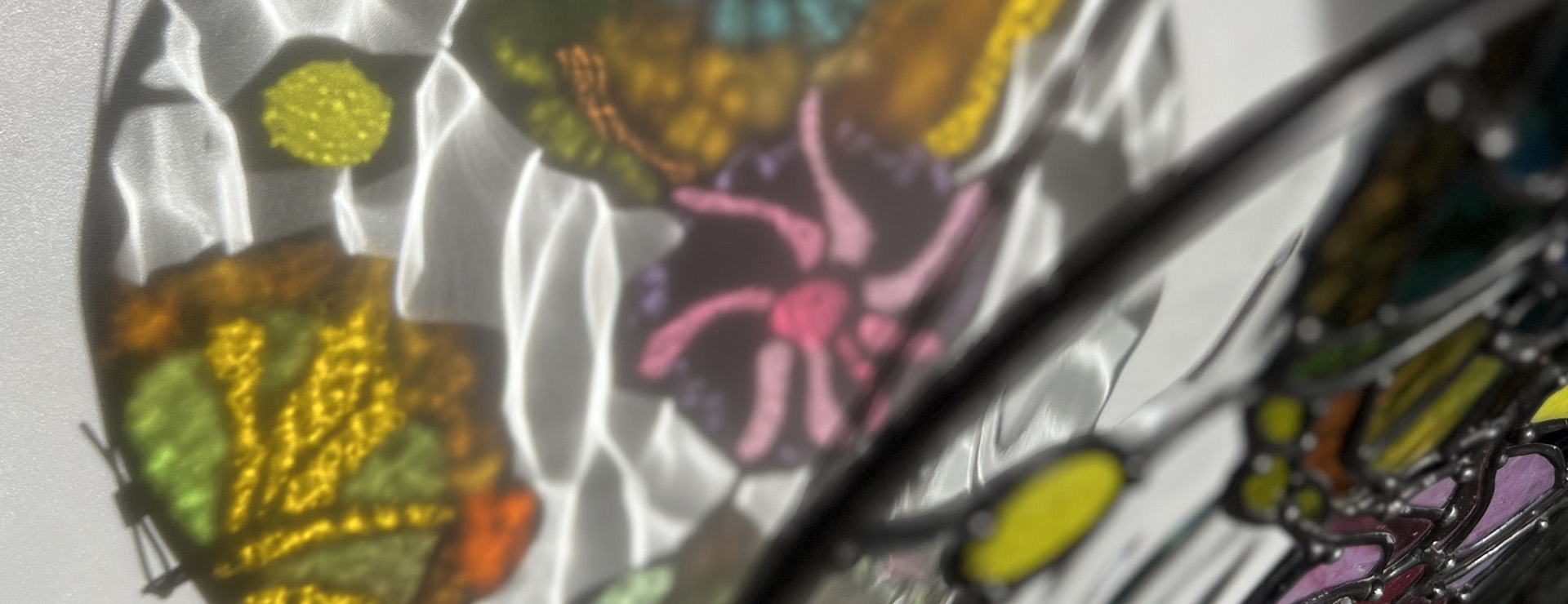 A side-by-side of stained glass piece with its  refraction featuring various colours and textures of glass.