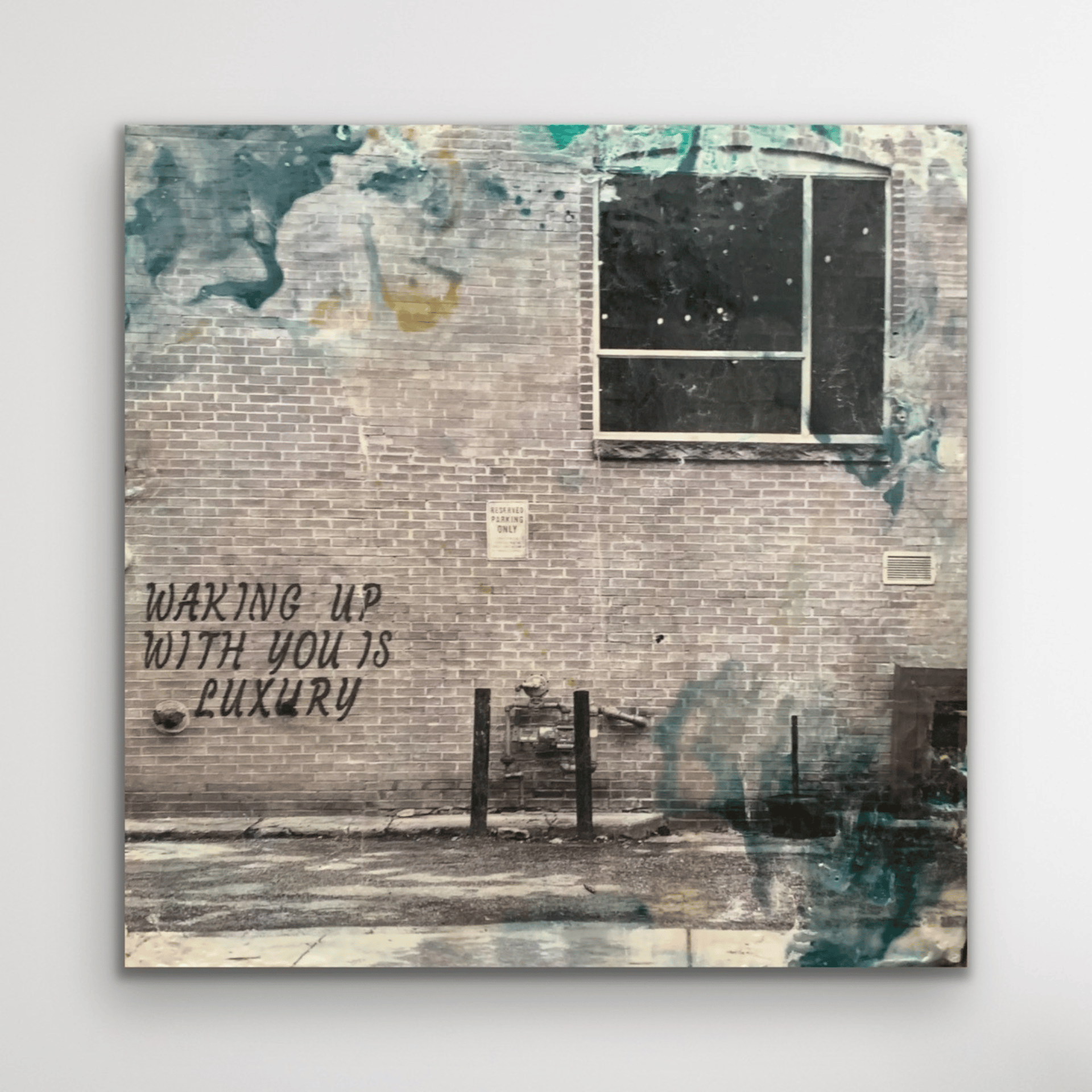 Black and white photograph of the text 
"Waking up with you is luxury" on a brick wall. Spatters of paint and encaustic wax surround the image. 
