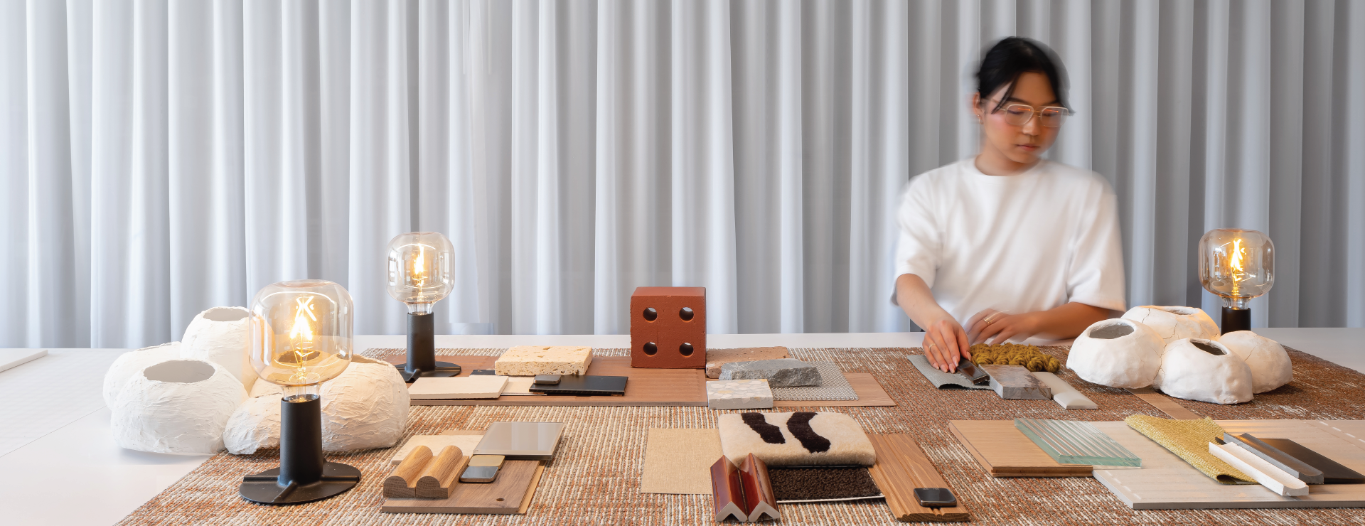 Interior Designer Paul Lee behind a table of materials and lighting fixtures, in the Mason Studio office.