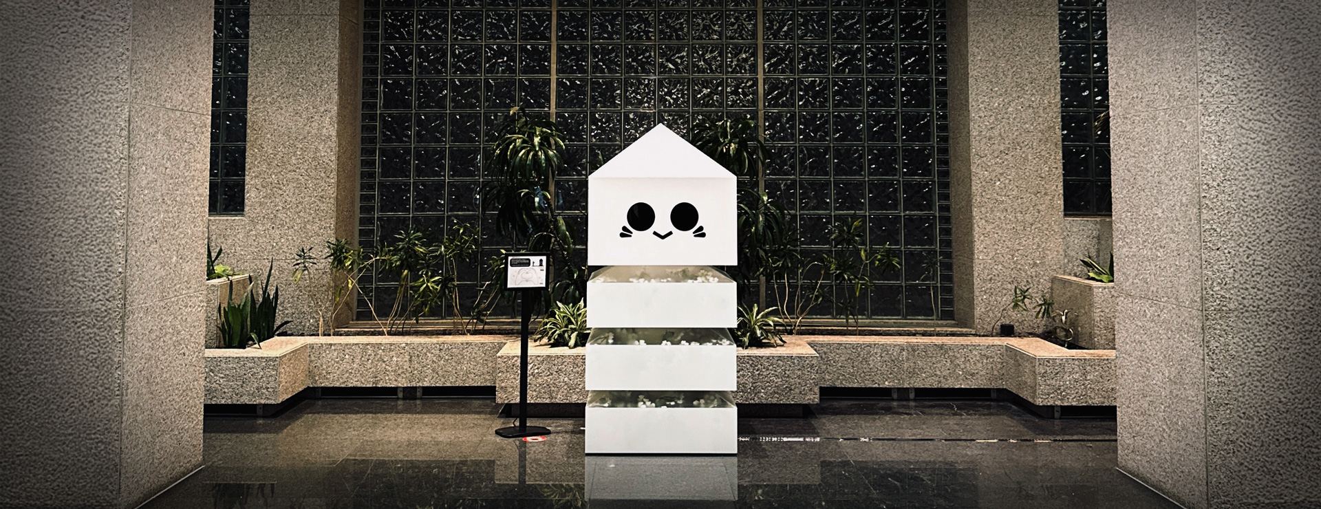 A 3 tiered installation with a calm face stands in front of a lake with a clear blue sky. 