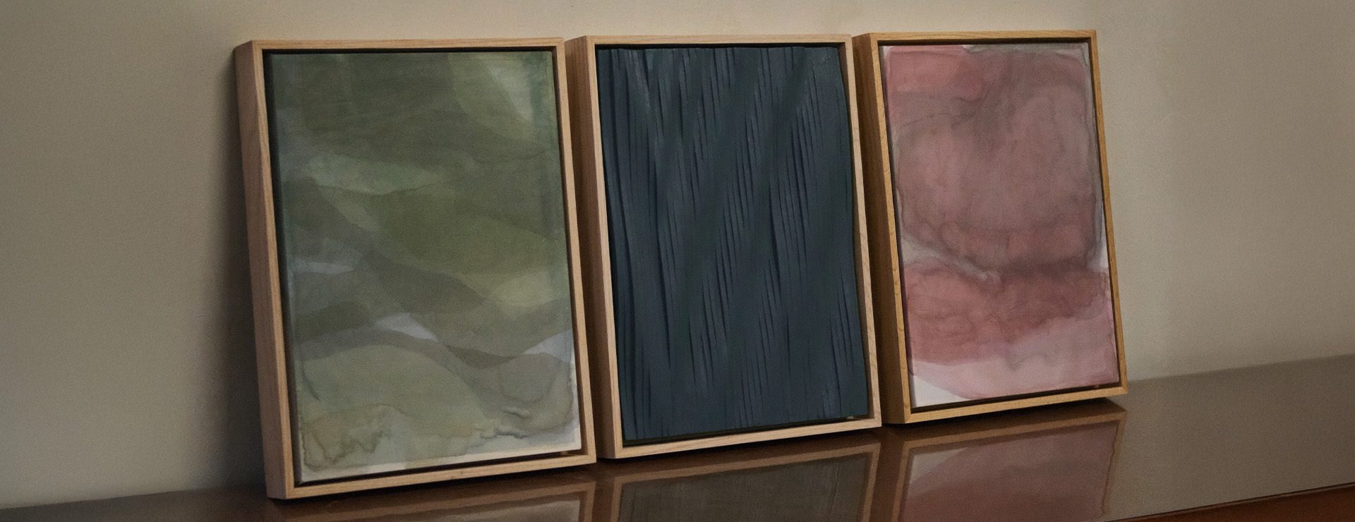 Two pieces of art hang on a blank wall. The left one is made out of wood that has been sculpted into a wave form. The right one has a 'fuzzy' paint application and resembles an abstracted flower.