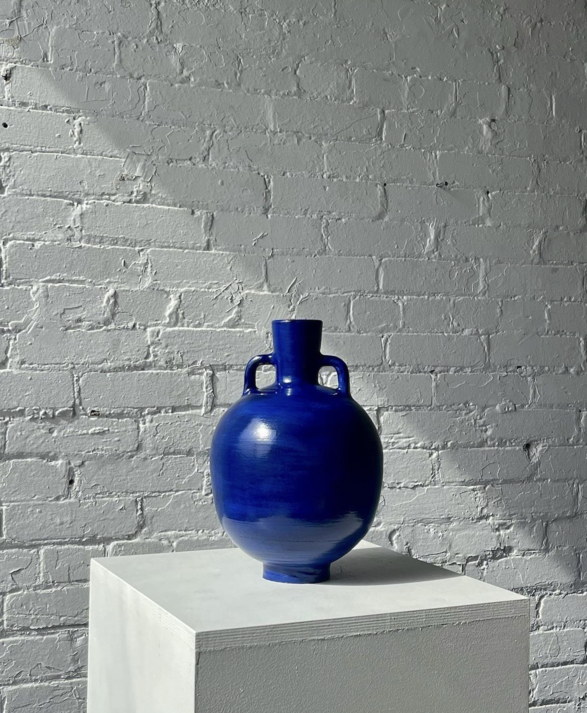 Round dark blue vase on plinth in front of white brick wall