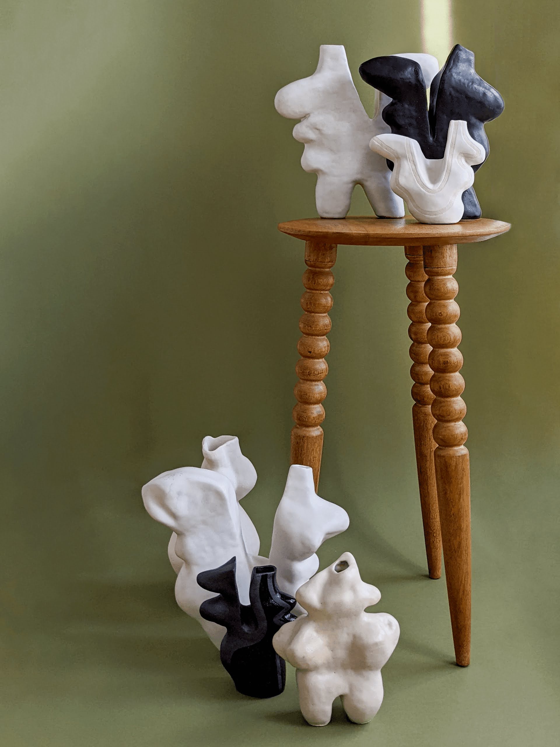 A stool with group of black & white ceramic vessels on it, and at the foot