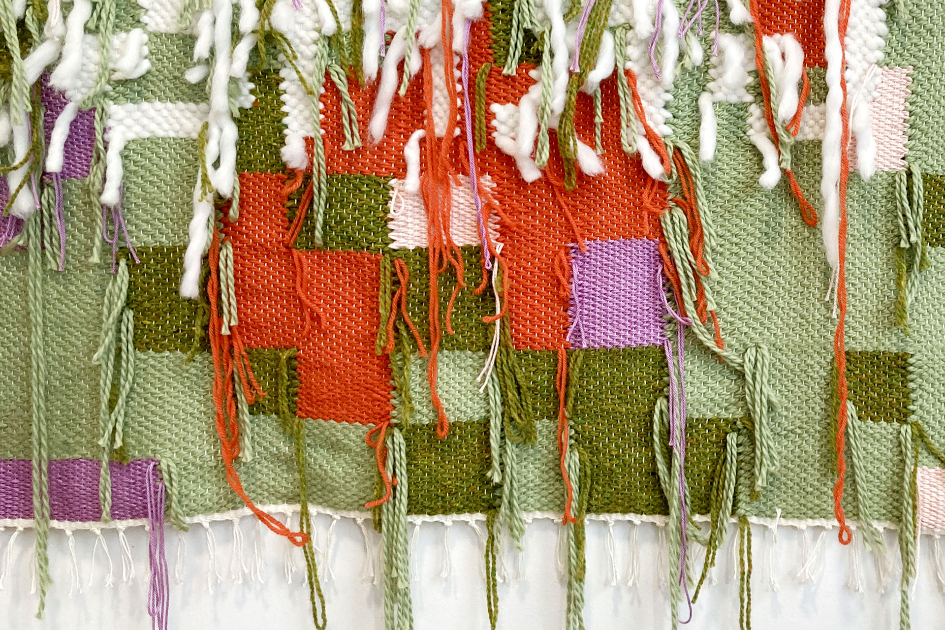 A detail shot of the back of a woven textile that has the colours green, purple, pink, red and white.