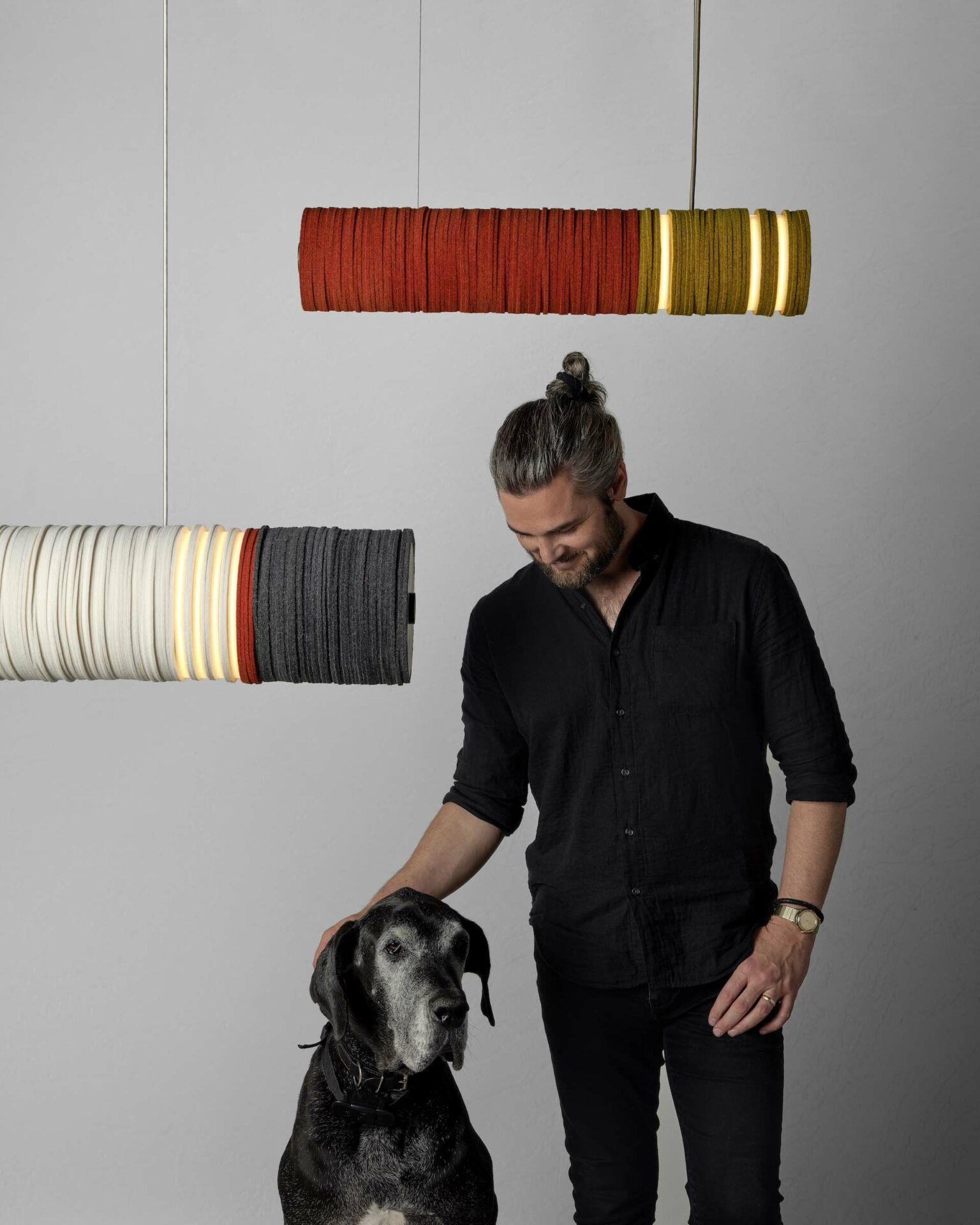 A man wearing black petting a dog under felt pendant lights