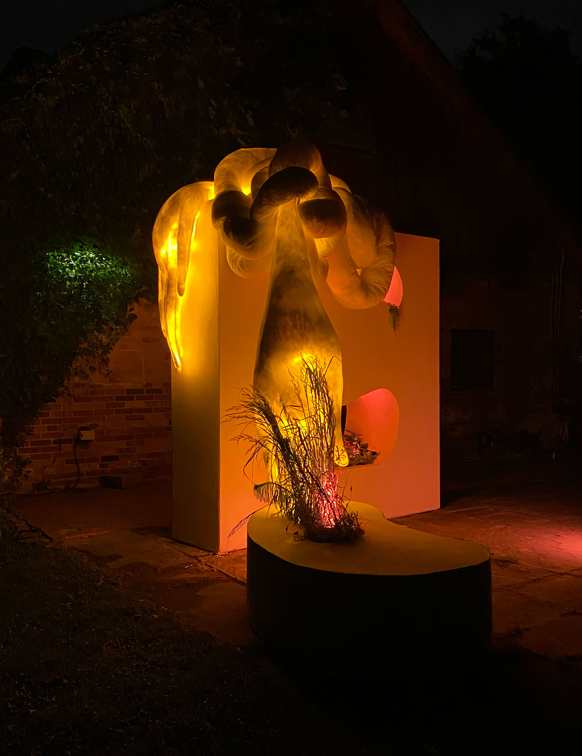 Intertwined soft sculpture in the form of long arms with plants glowing with orange light