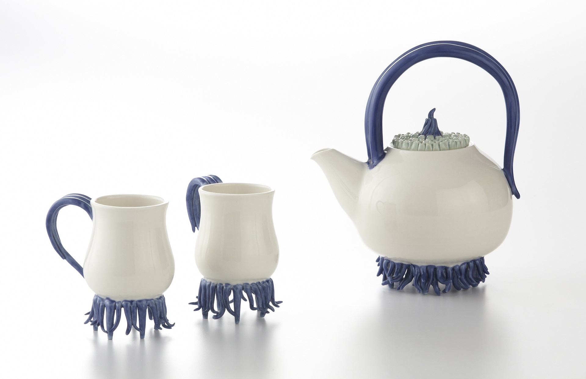 White teapot and two cups with sculptural blue tentacles as handles and feet on each of the pieces