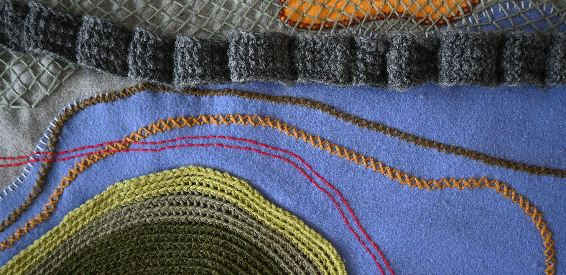 Detail shot of the textile map, showing multi-coloured hand stitching, as well as green and gray wool appliques.