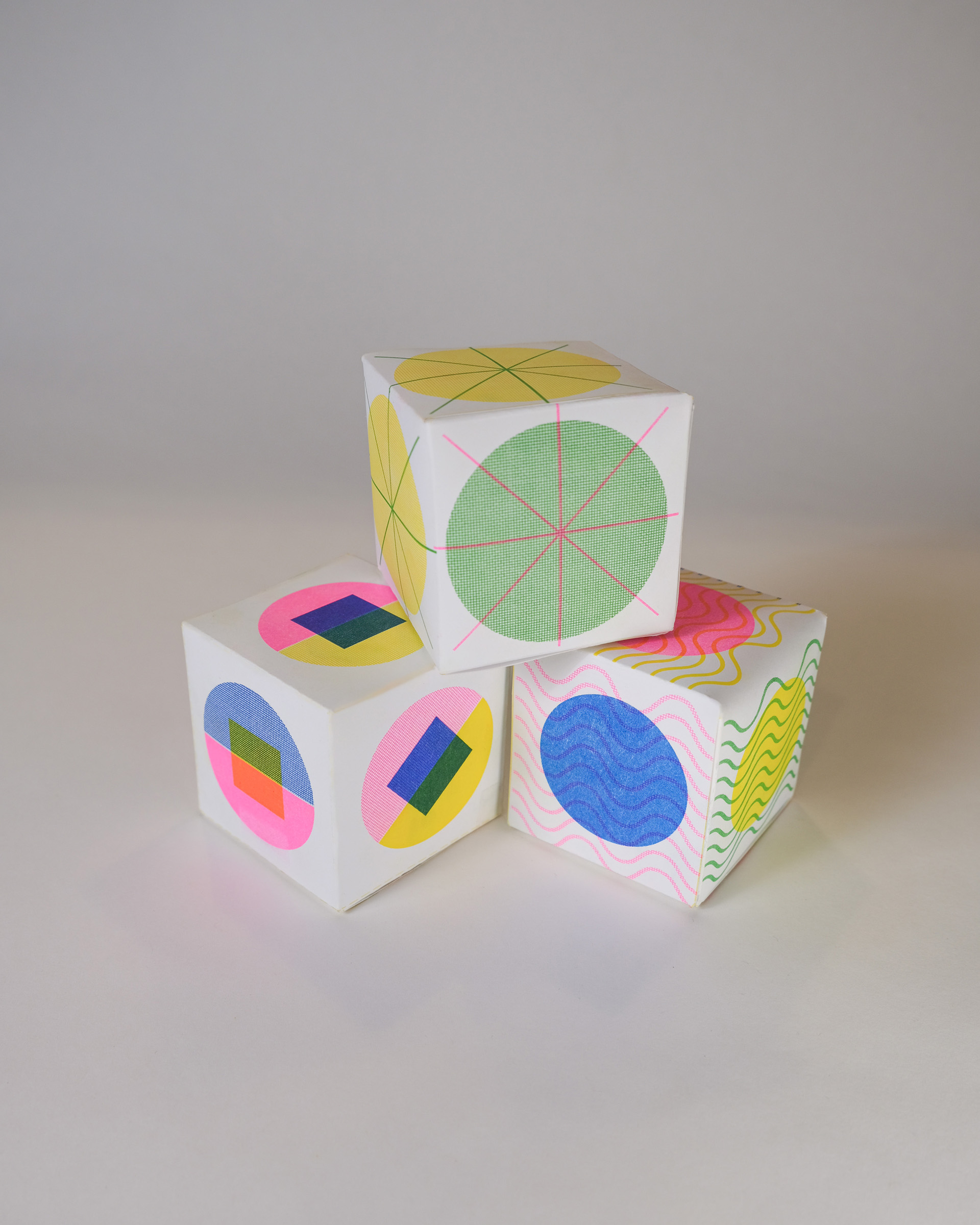 Three paper cubes stacked in a pyramid which are risograph printed with geometric shapes