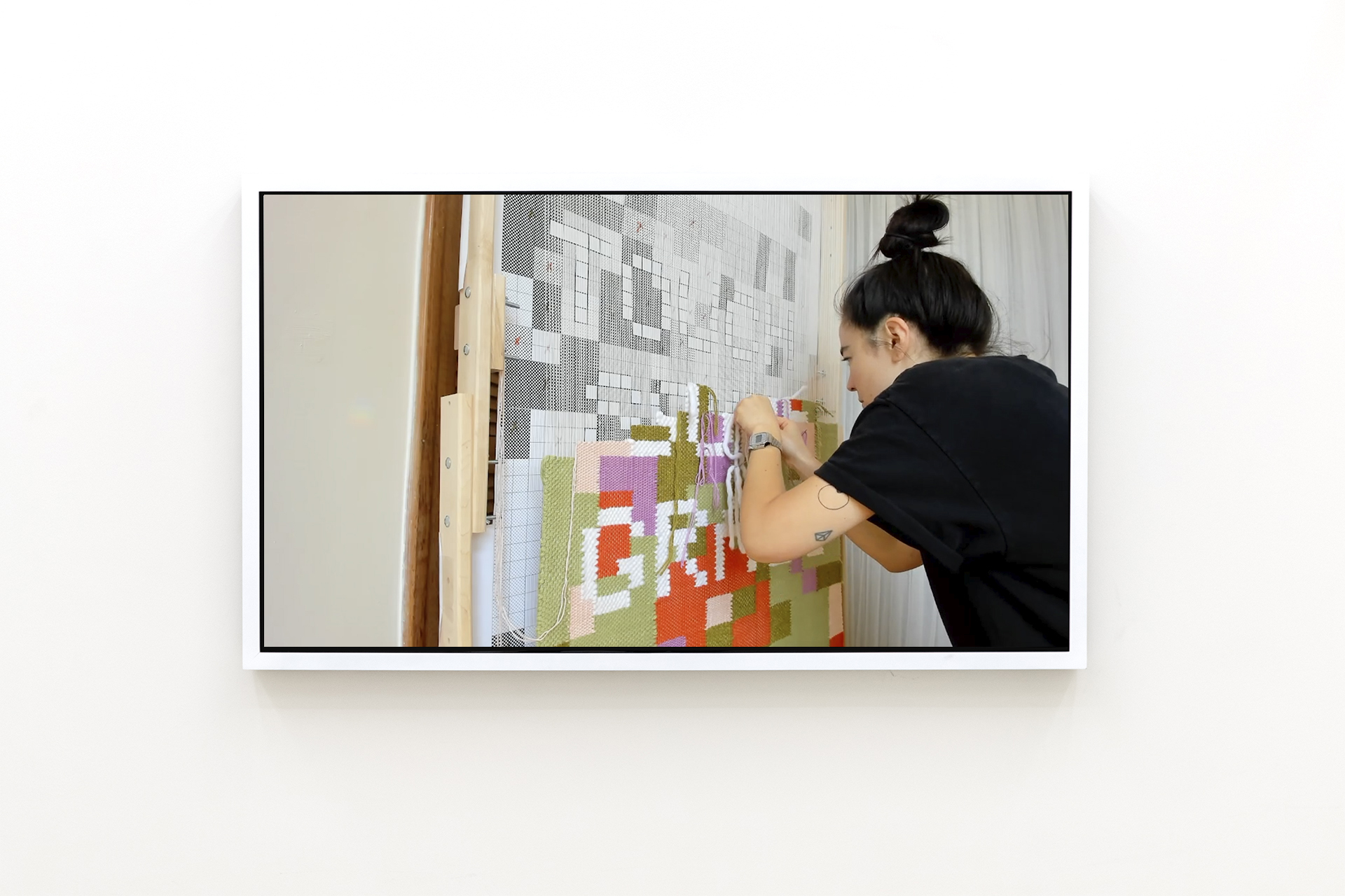 A video screen mounted on the wall showing the process of making the hand woven textile.