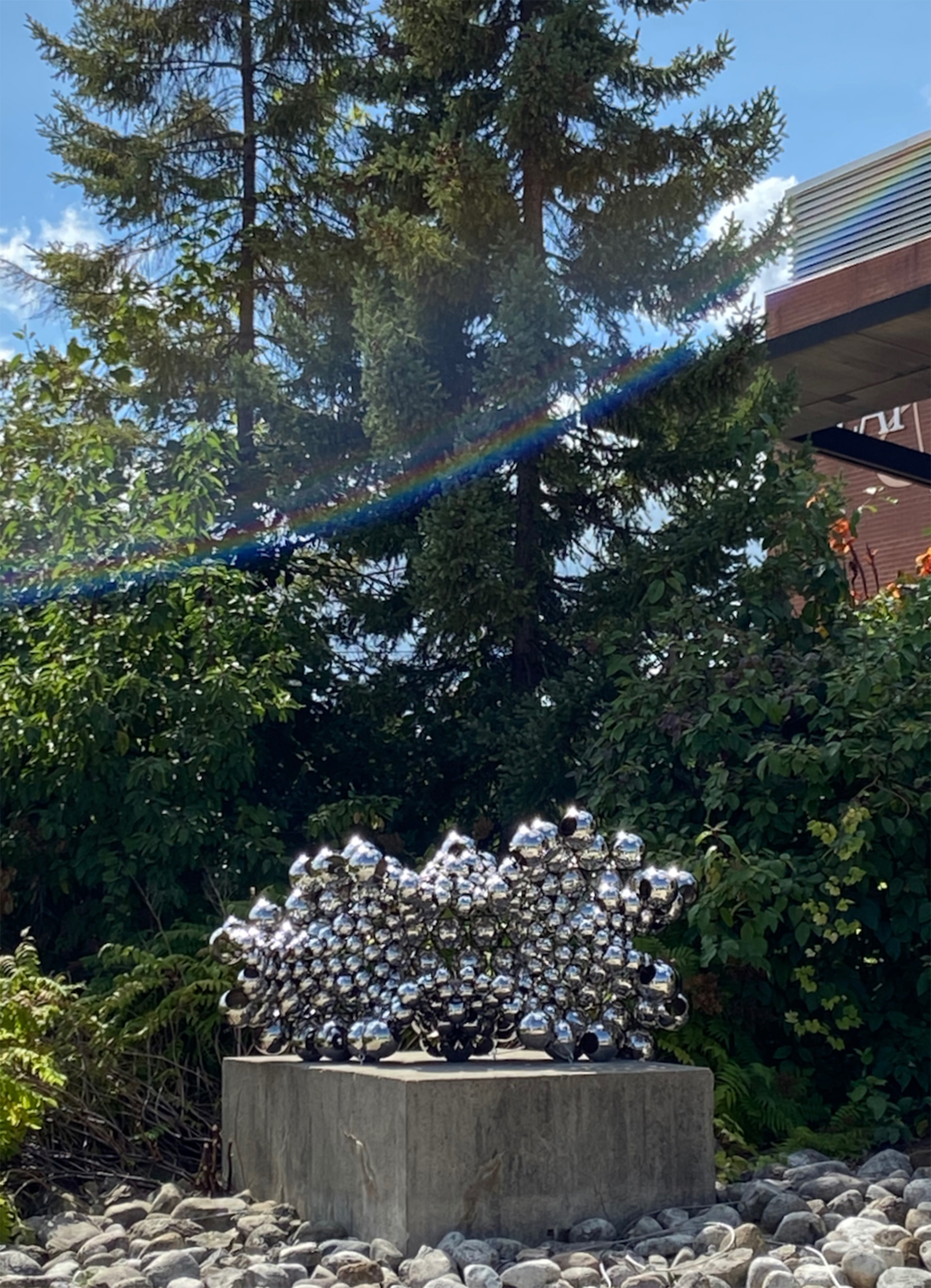 abstract sculpture using stainless steel spheres in front of green trees